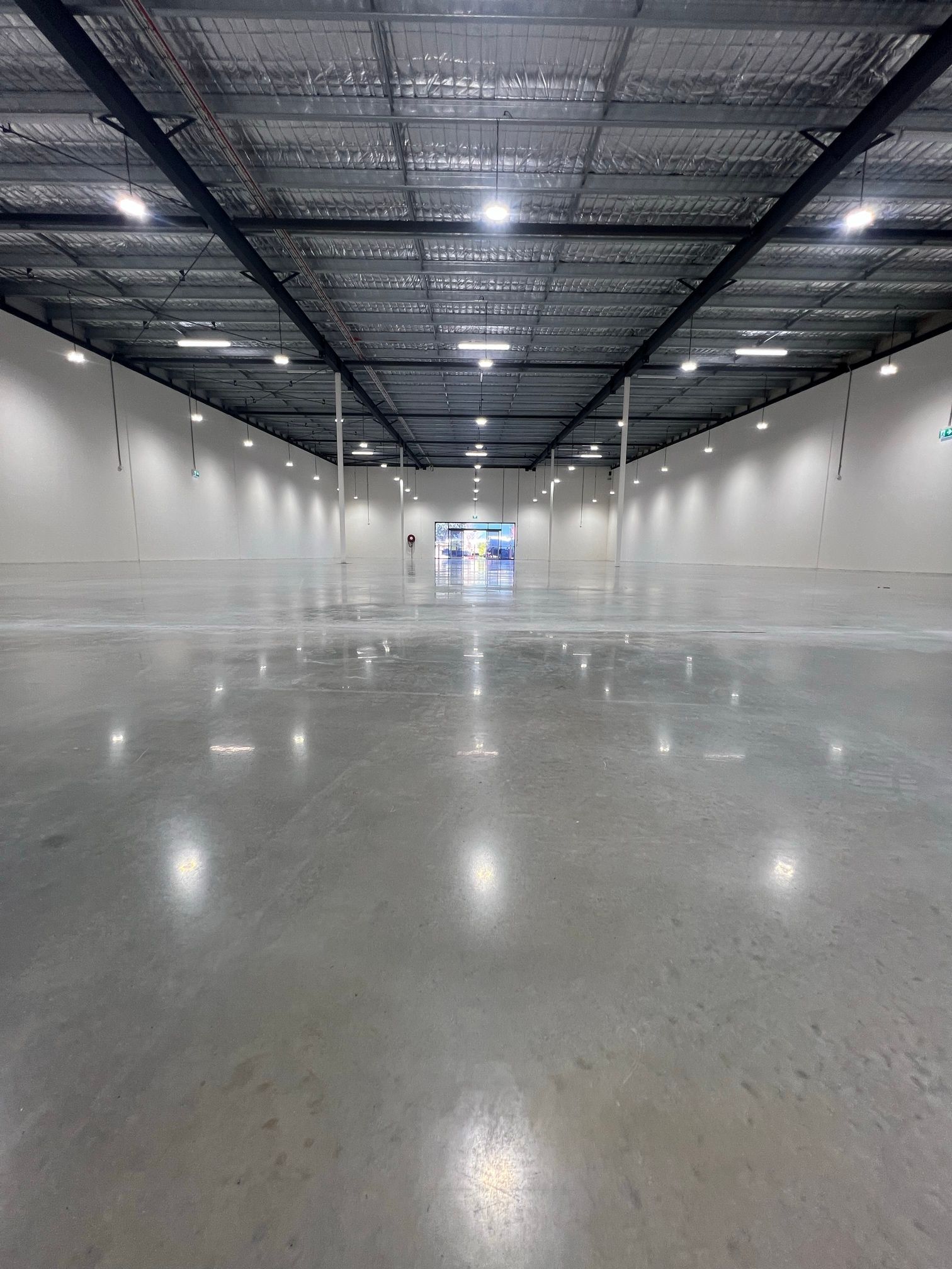 Empty warehouse interior with polished concrete floor, white walls, and overhead lights reflected on the floor
