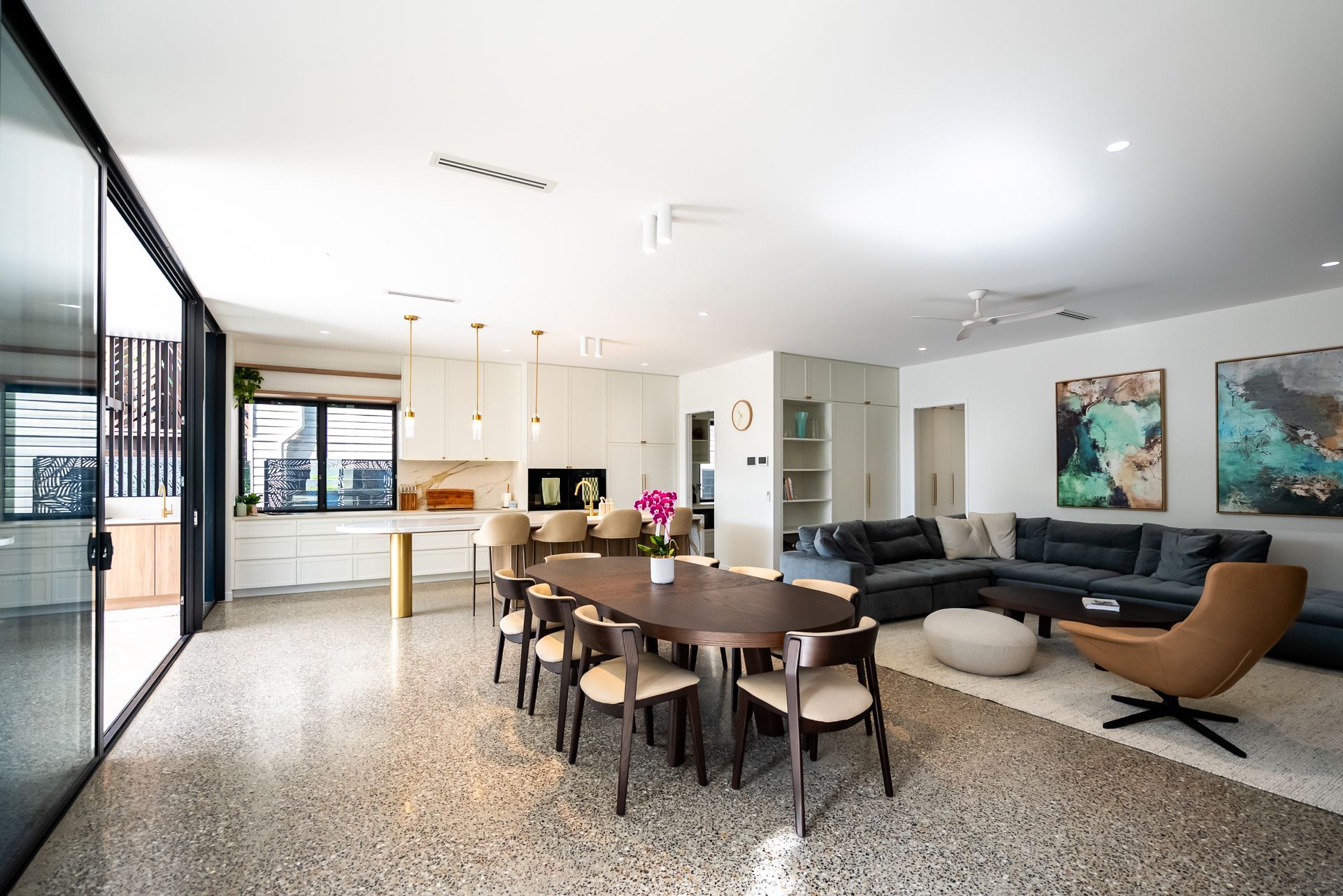 Modern open-plan living room with dining table, dark sofas, and colorful wall art in a bright interior