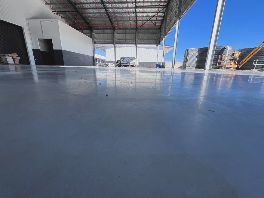 Empty industrial warehouse with a shiny blue floor and stacked pallets near an open bay door