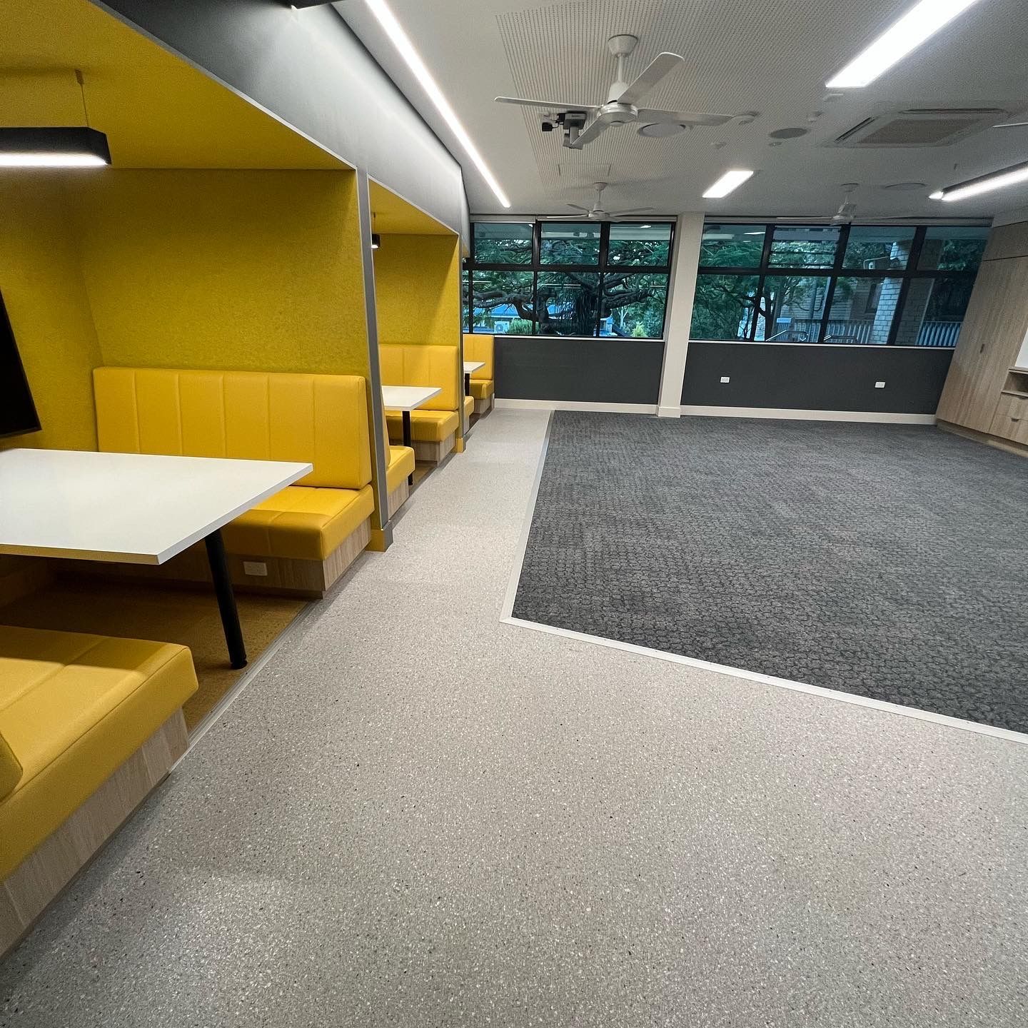 Modern office lounge with yellow booths, white tables, and a gray carpeted open area.