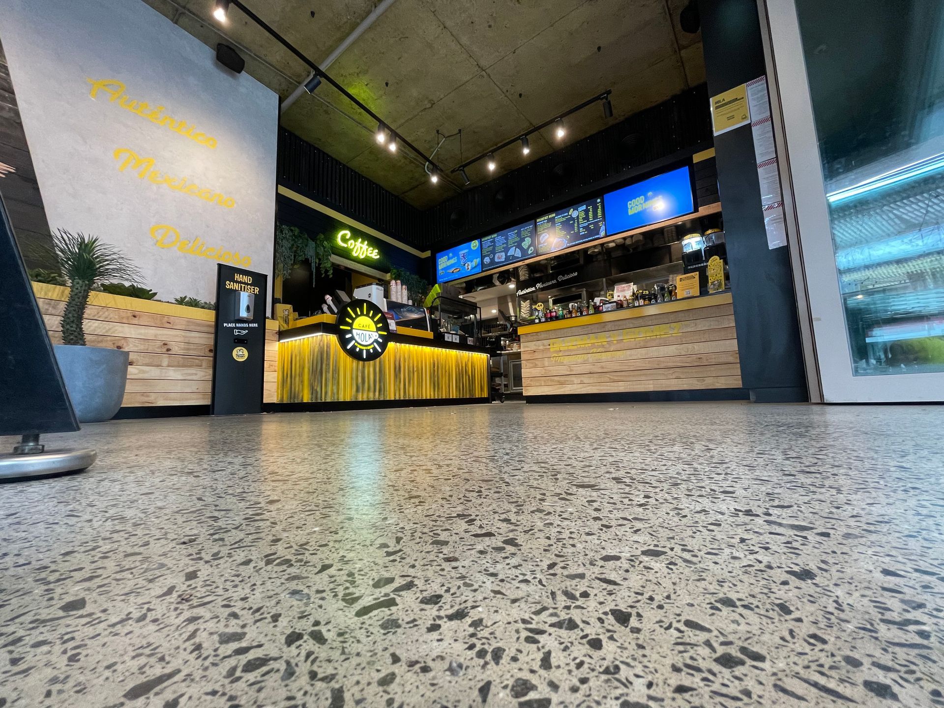 Empty modern café interior with a yellow counter, stone walls, and a speckled floor