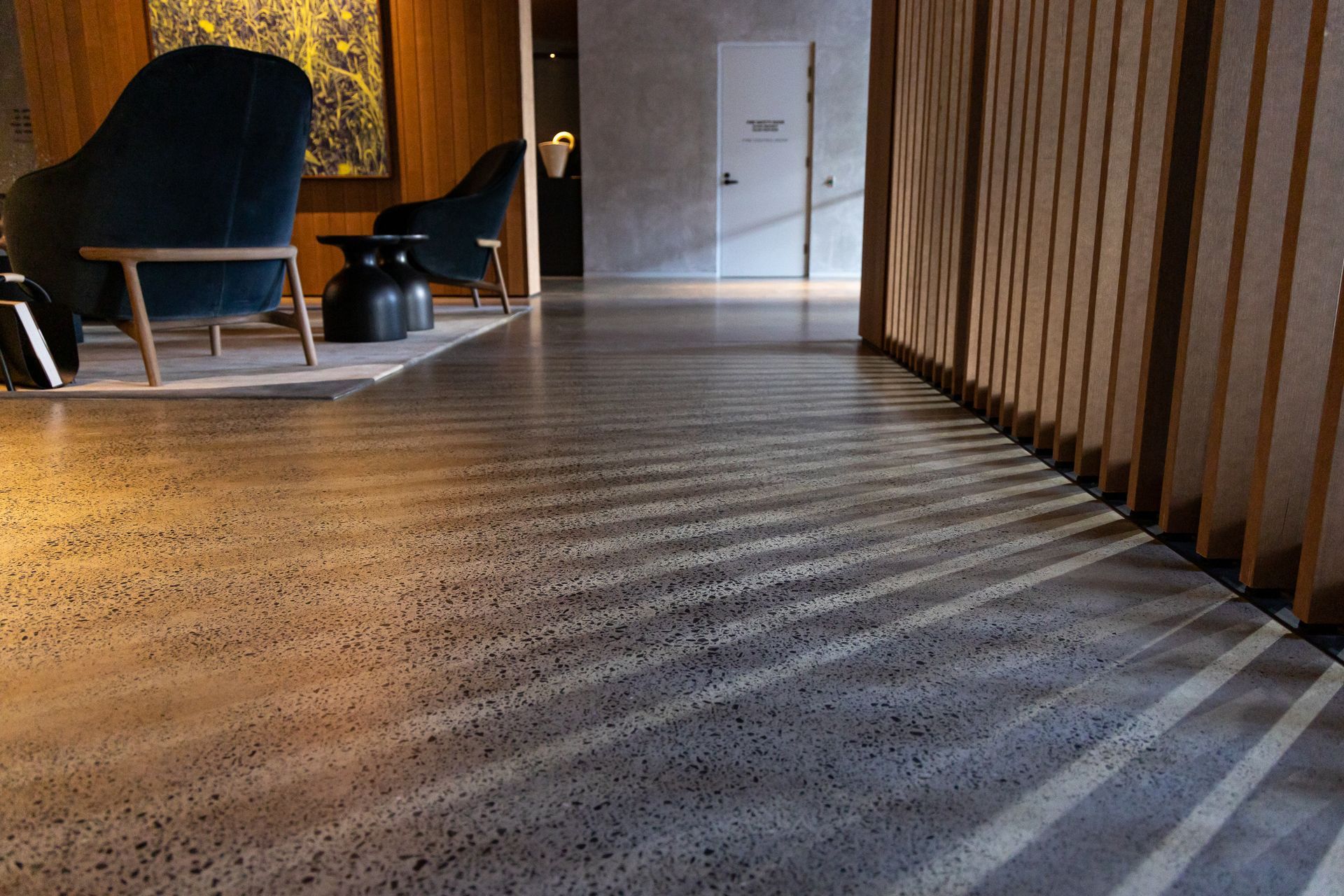 Dim hallway with patterned carpet, wooden slat wall, and lounge chairs in the background.