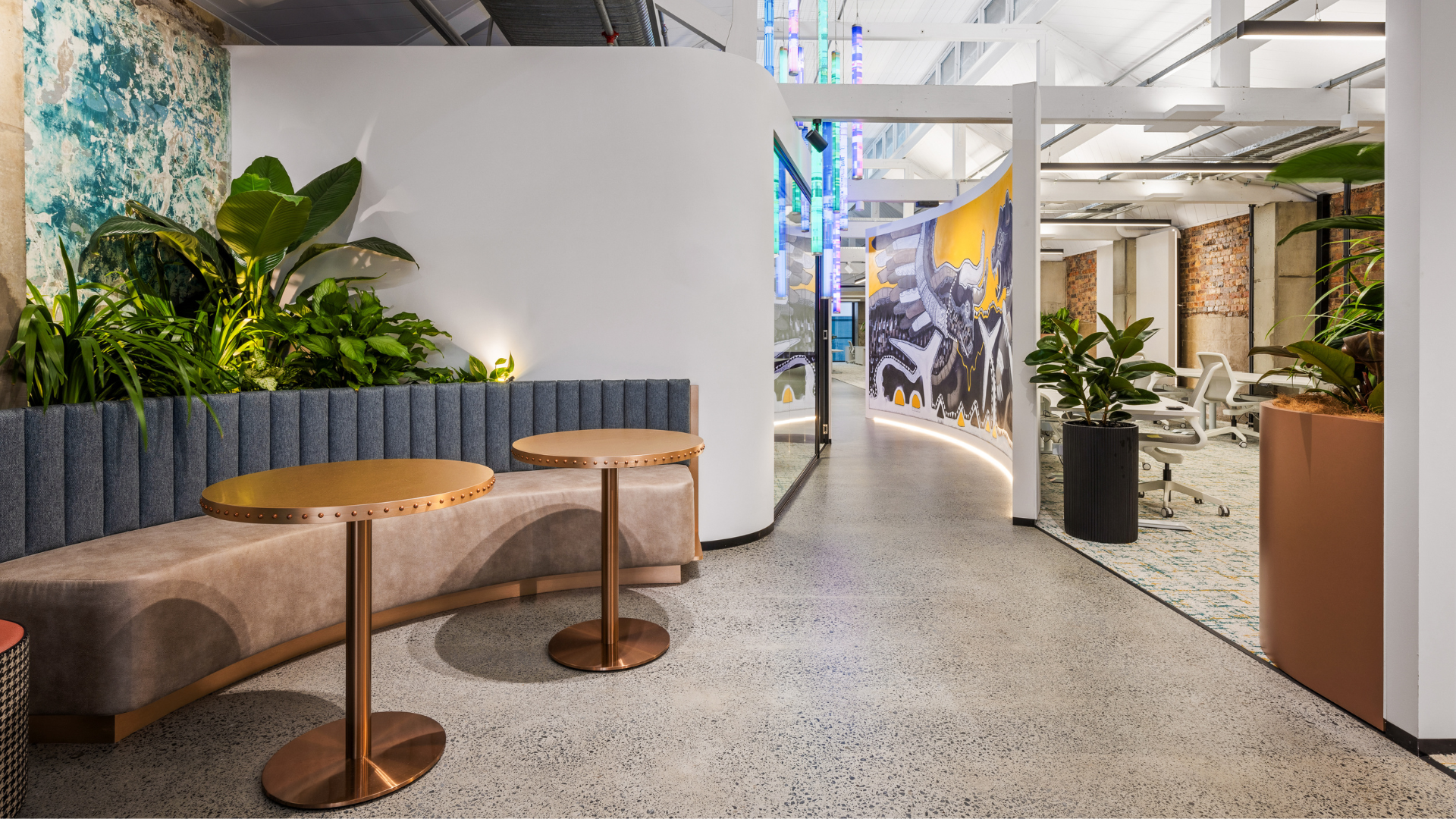 Modern office lounge with curved beige bench, round tables, plants, and a bright hallway view Modern office lounge with curved beige bench, round tables, plants, and a bright hallway view