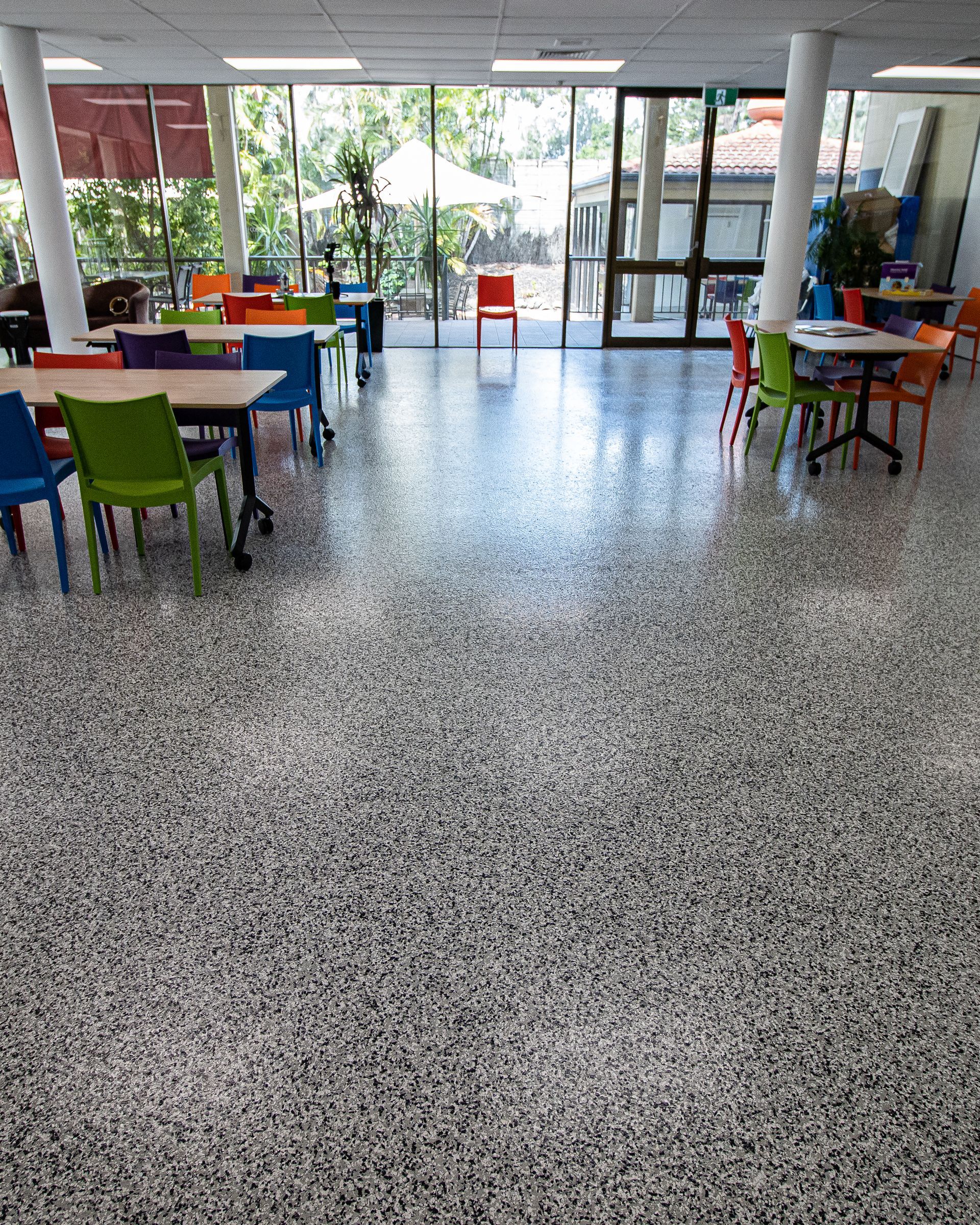 Bright classroom or cafeteria with colorful chairs and tables on a polished floor, empty and sunlit