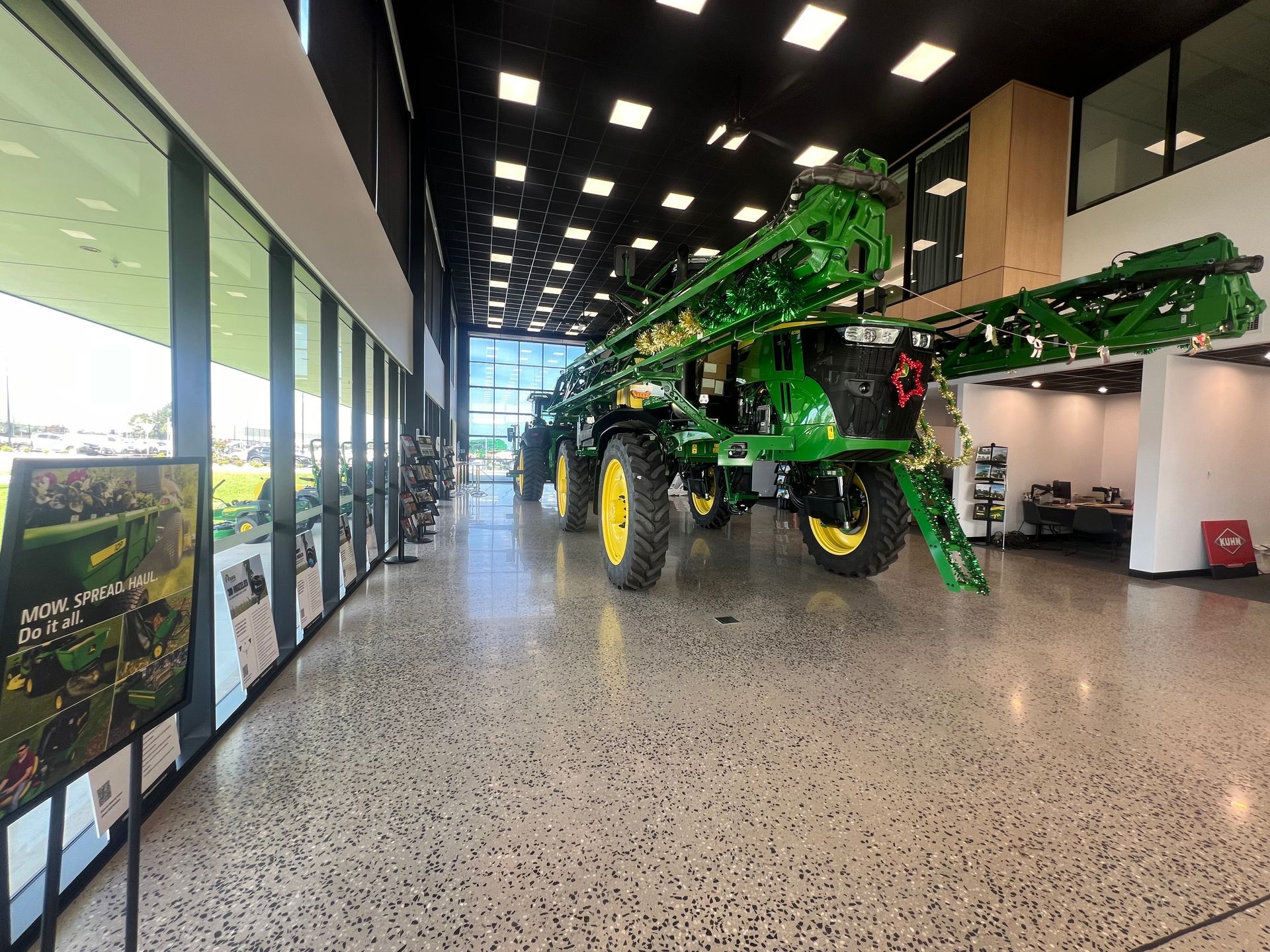 Large green agricultural sprayer displayed in a bright showroom with floor-to-ceiling windows