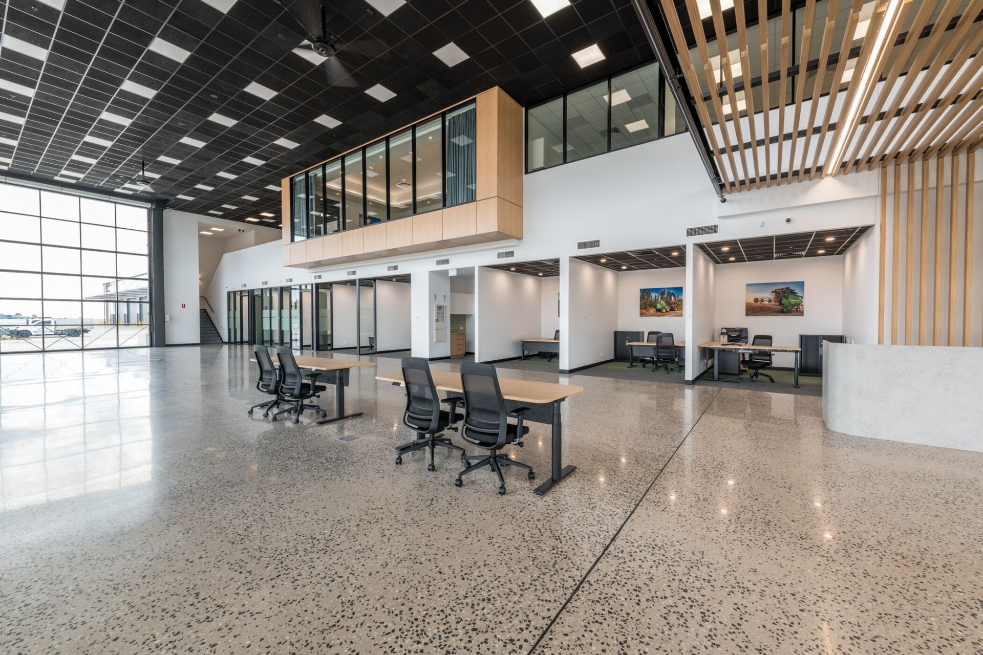 Modern office lobby with glass walls, desks, chairs, and polished terrazzo floor