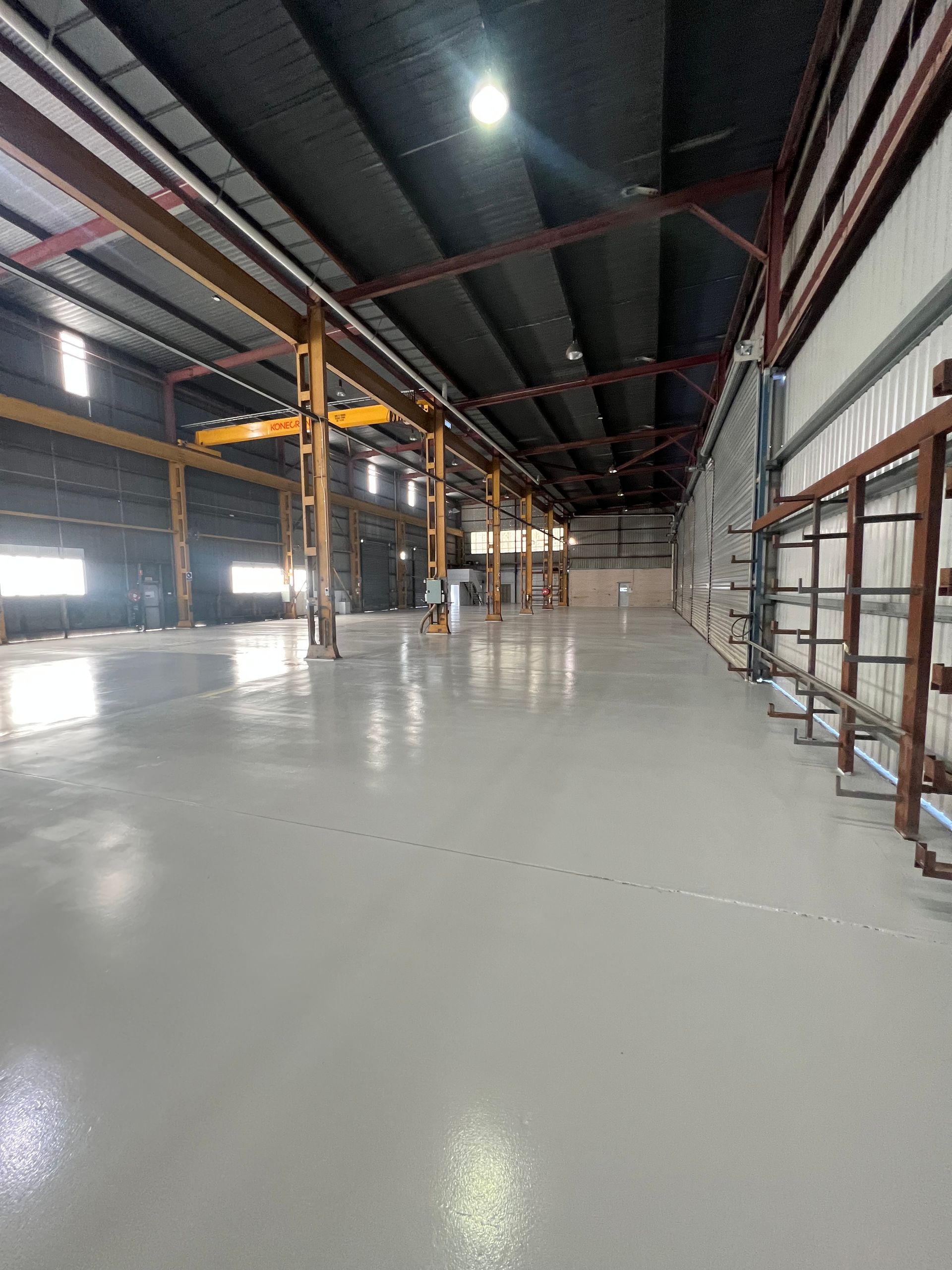 Empty industrial warehouse with glossy concrete floor, high ceiling, and rows of windows and steel beams