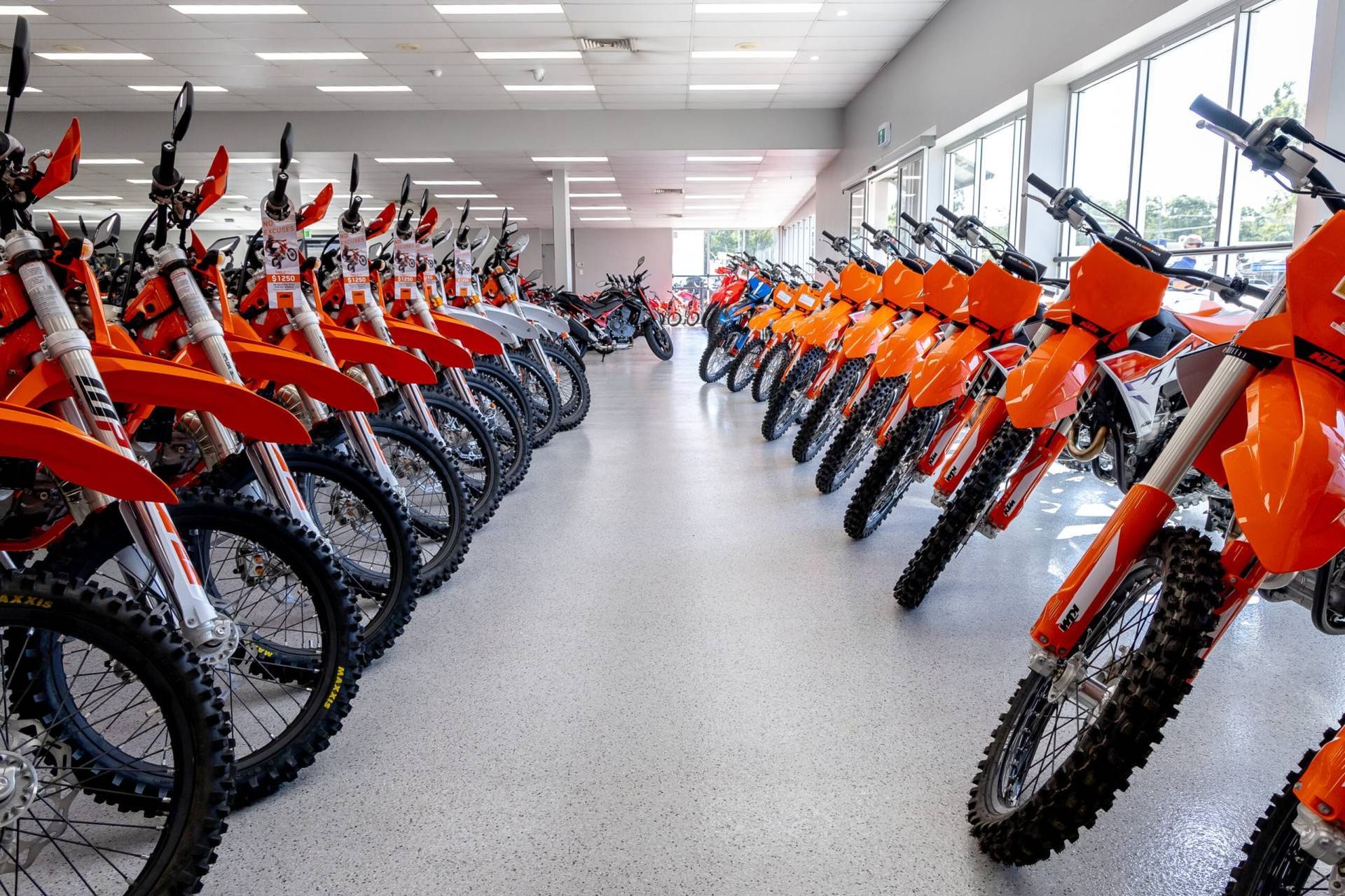 Rows of orange and black dirt bikes lined up inside a showroom or warehouse