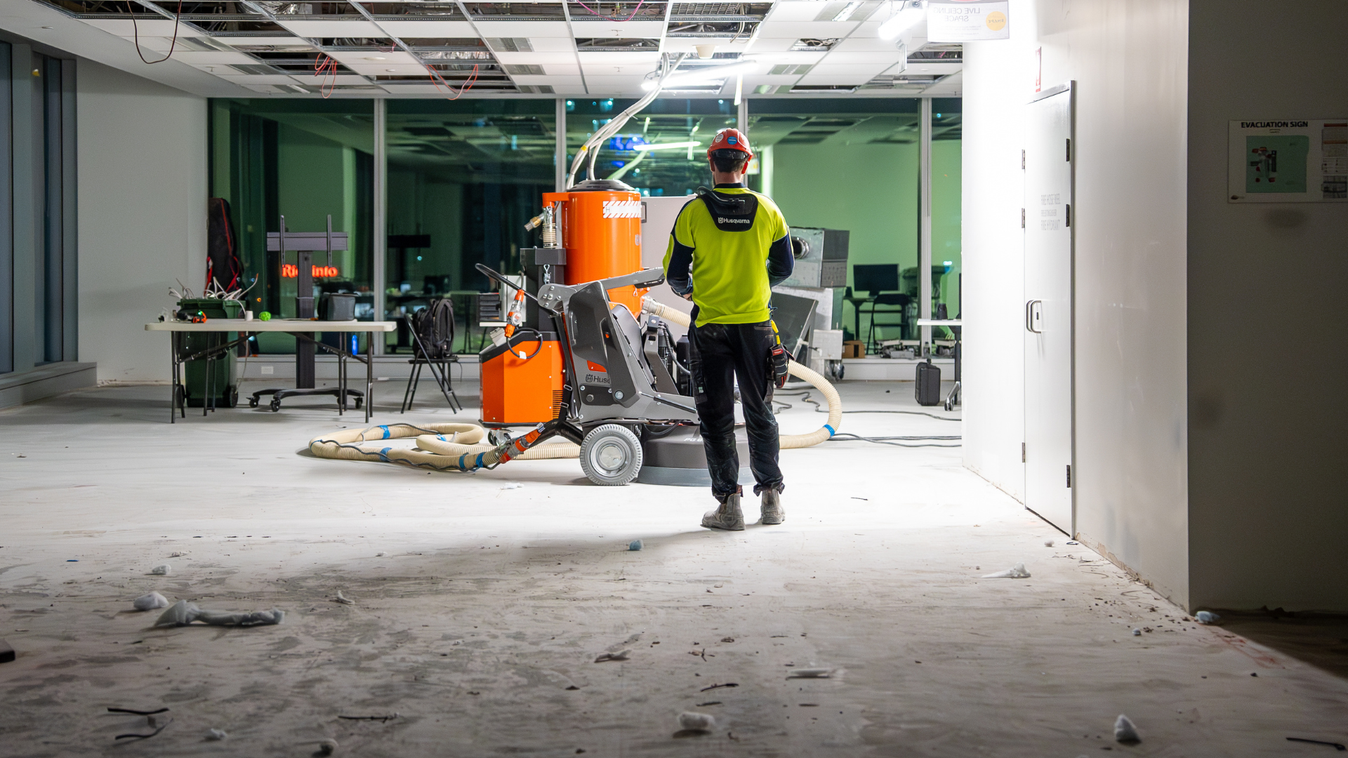 Construction worker in neon vest walking through a dusty unfinished indoor space with equipment nearby Construction worker in neon vest walking through a dusty unfinished indoor space with equipment nearby