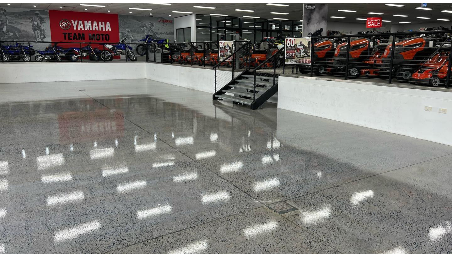 Showroom with polished gray floor and rows of motorcycles behind a white barrier under bright lights