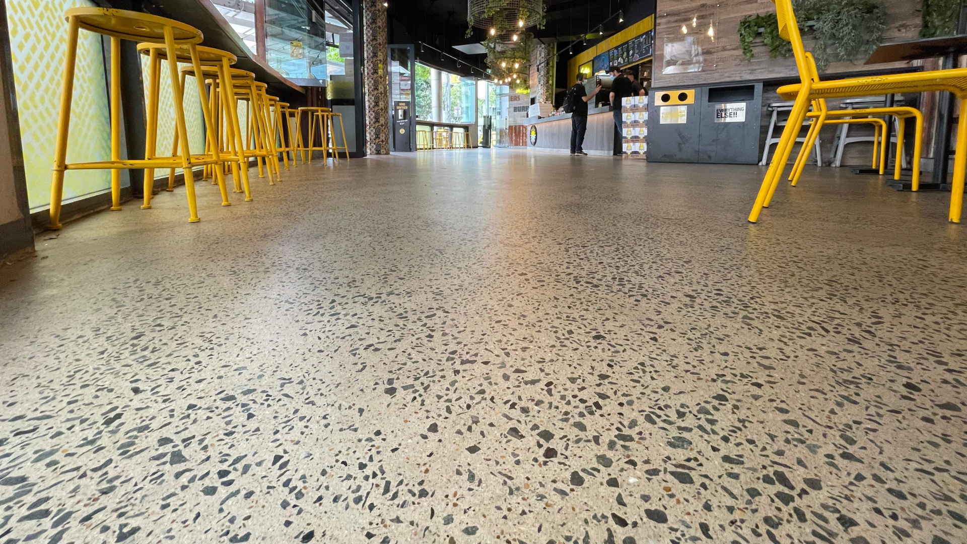 Empty café interior with yellow stools and a speckled terrazzo floor, viewed from low angle Empty café interior with yellow stools and a speckled terrazzo floor, viewed from low angle