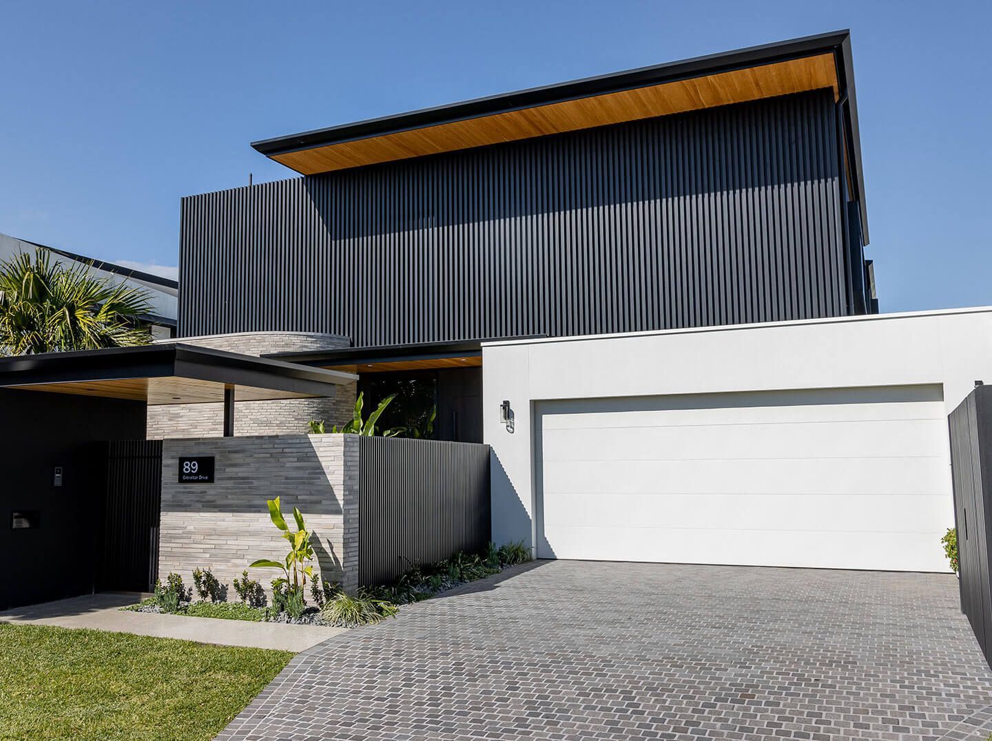 Modern two-story house with dark siding, white garage, and cobblestone driveway