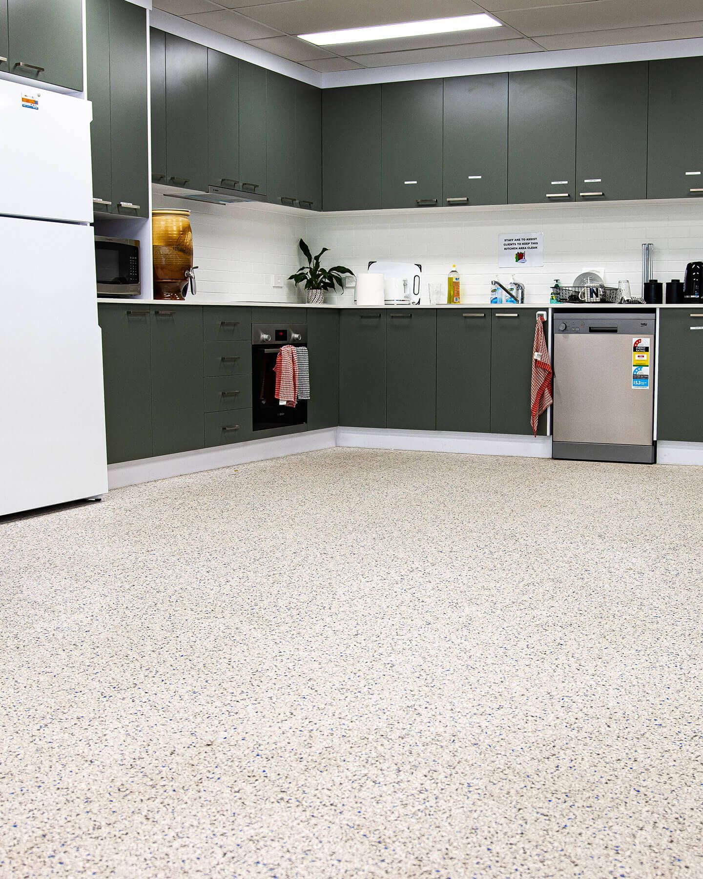 Commercial kitchen with green cabinets, white fridge, stainless sink, and speckled floor