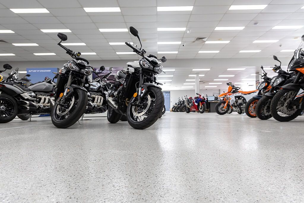 Motorcycles lined up in a bright showroom with a speckled floor and ceiling lights