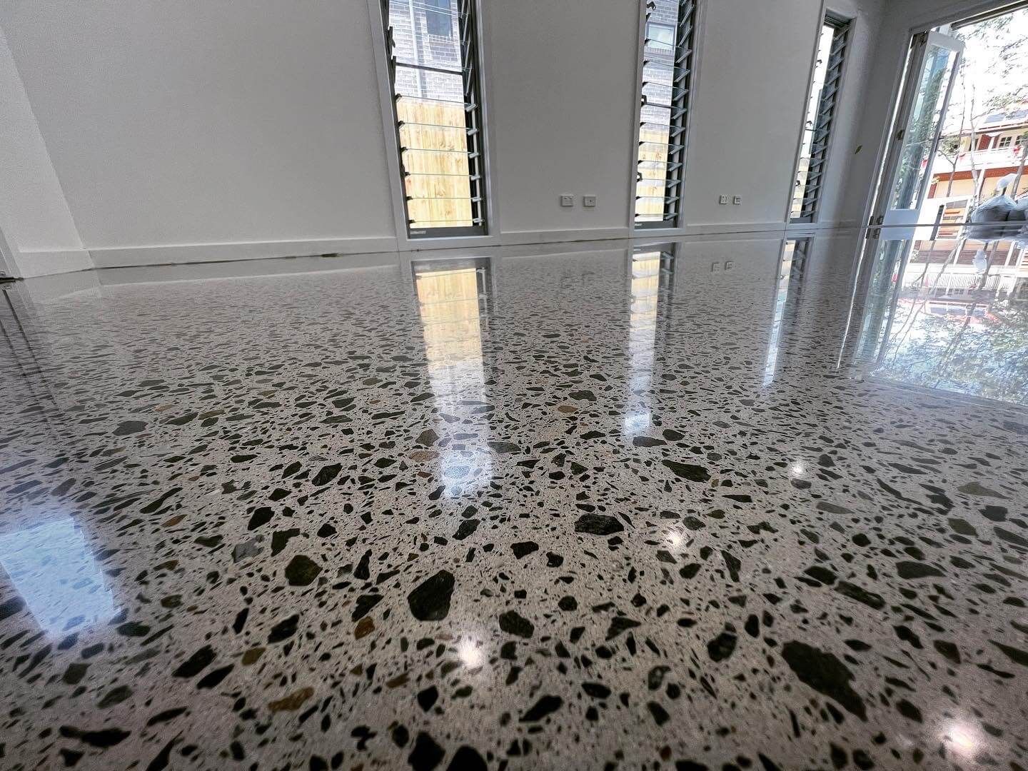 Modern room with polished terrazzo floor, white walls, and tall narrow windows reflecting light.