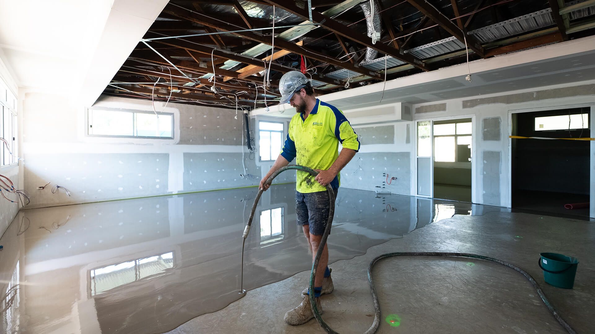 Worker in neon safety vest using a hose to clean a flooded room under renovation