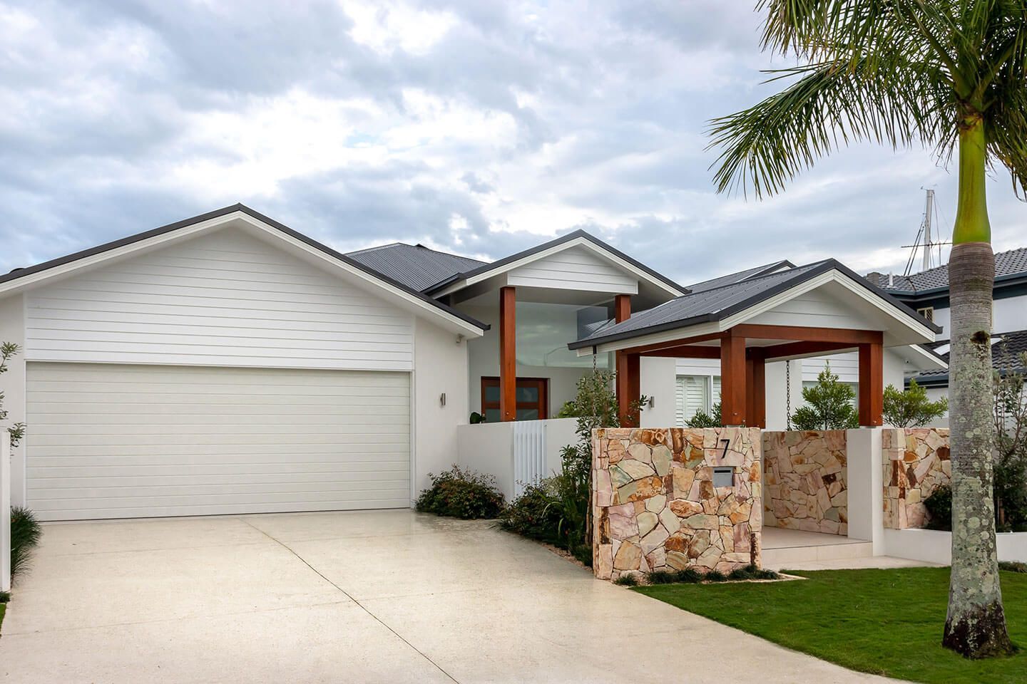 Modern white suburban house with a two-car garage, stone entry wall, and palm trees in front