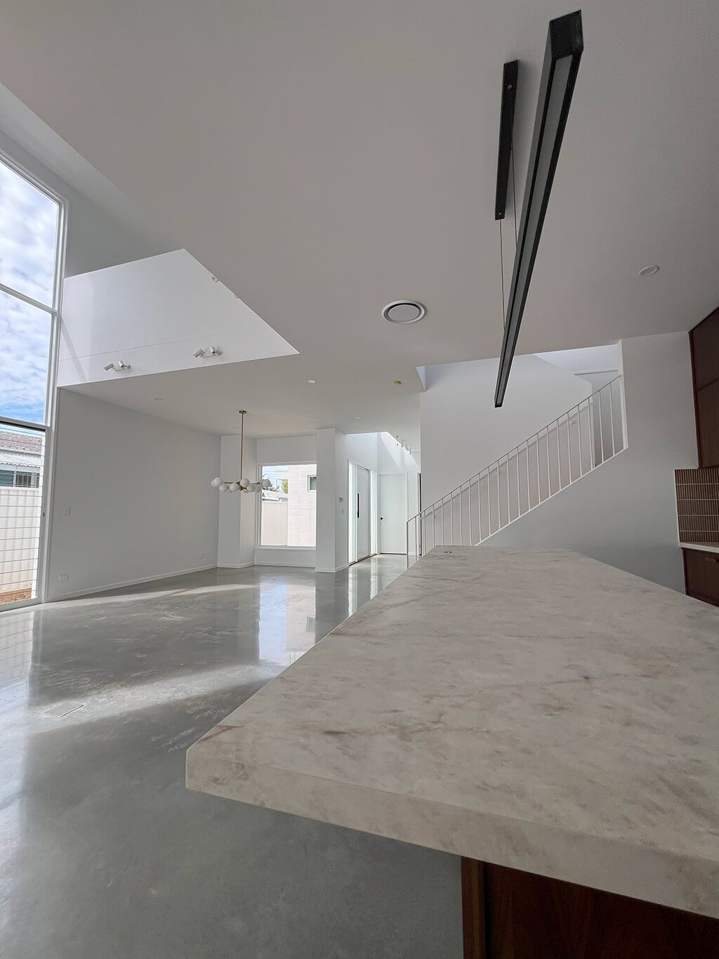 Modern open-plan interior with concrete floors, white walls, staircase, and large kitchen island