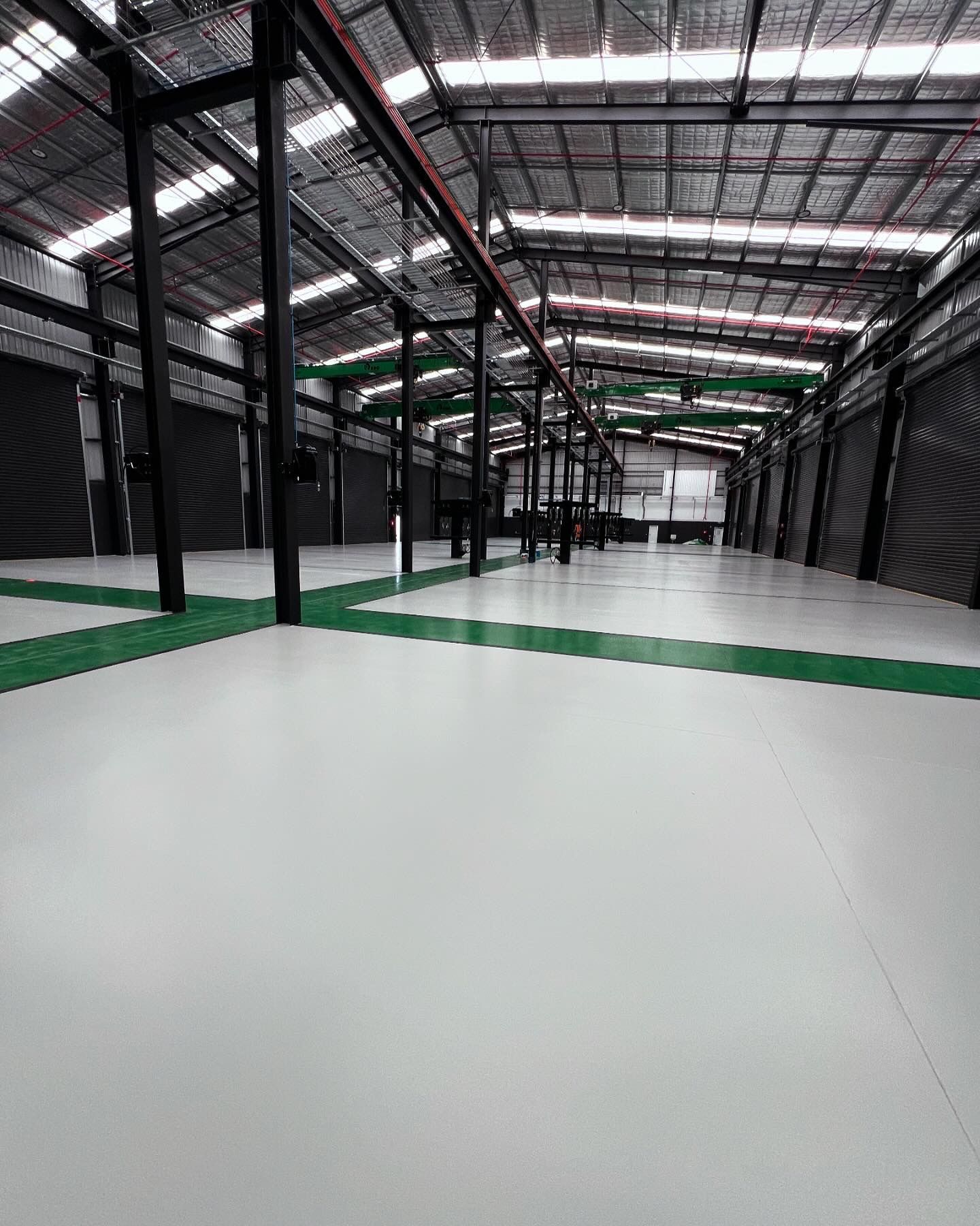 Empty warehouse interior with white floor, black columns, and green floor markings