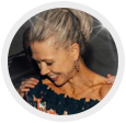 Profile photo of a smiling woman in a floral off-shoulder top, looking down against a dark background