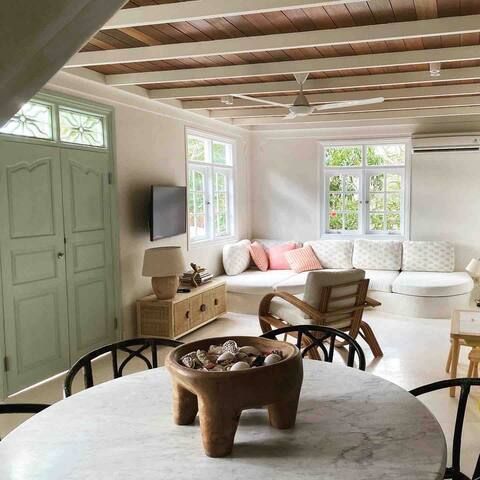 Bright, airy living space with light green door, white walls, wooden ceiling, and round marble table with decorative bowl.
