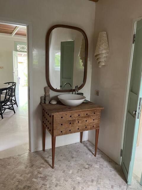 Bathroom with wooden vanity, oval mirror, and white sink. A doorway and a wall-mounted light fixture are also visible.