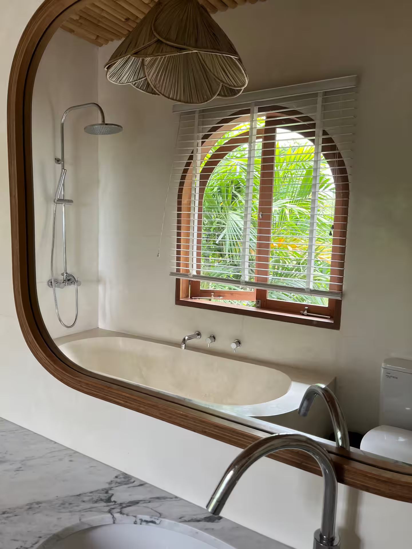 Bathroom with bathtub under a window, a shower, and a sink reflected in a mirror. The space has natural wood accents.