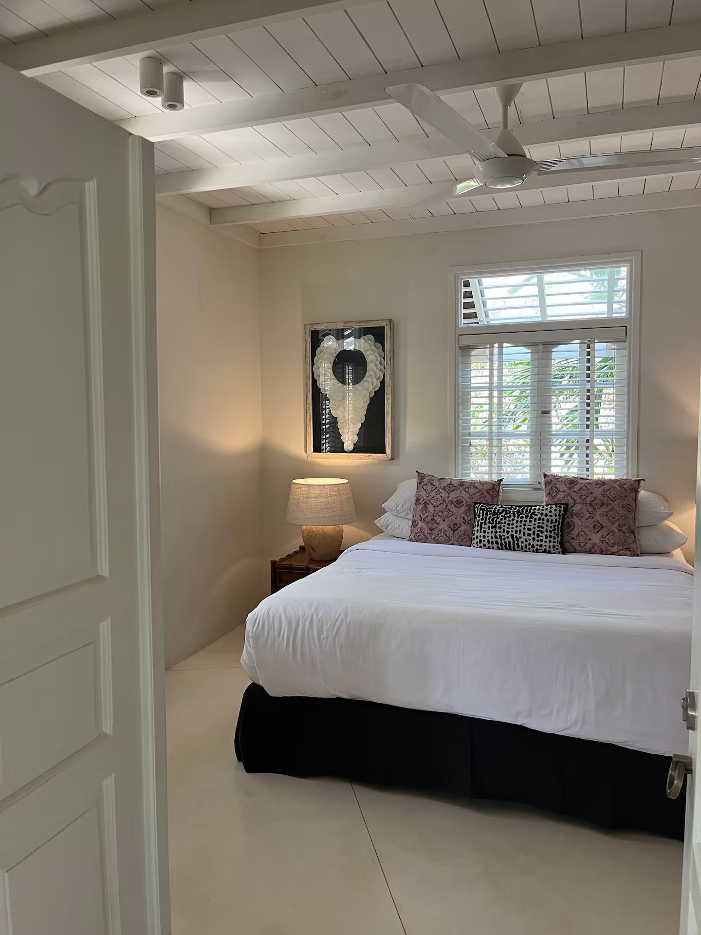 A bedroom with a white bed, pillows, and artwork; viewed from a partially open white door.