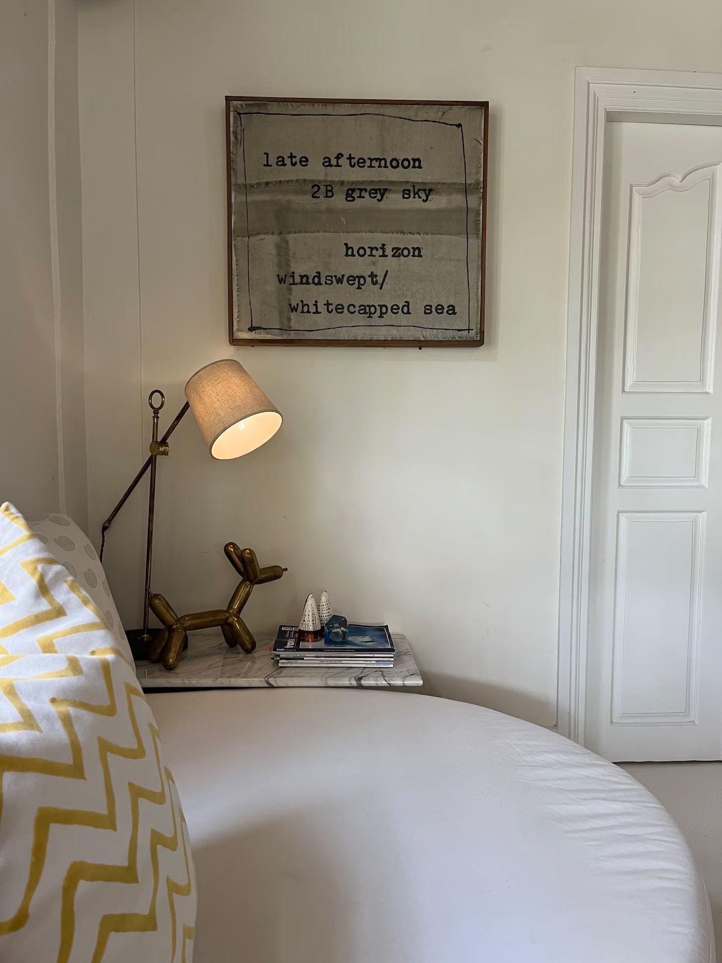 Bedroom with a round bed, nightstand, and lamp. Artwork hangs above the nightstand; a door is on the right.