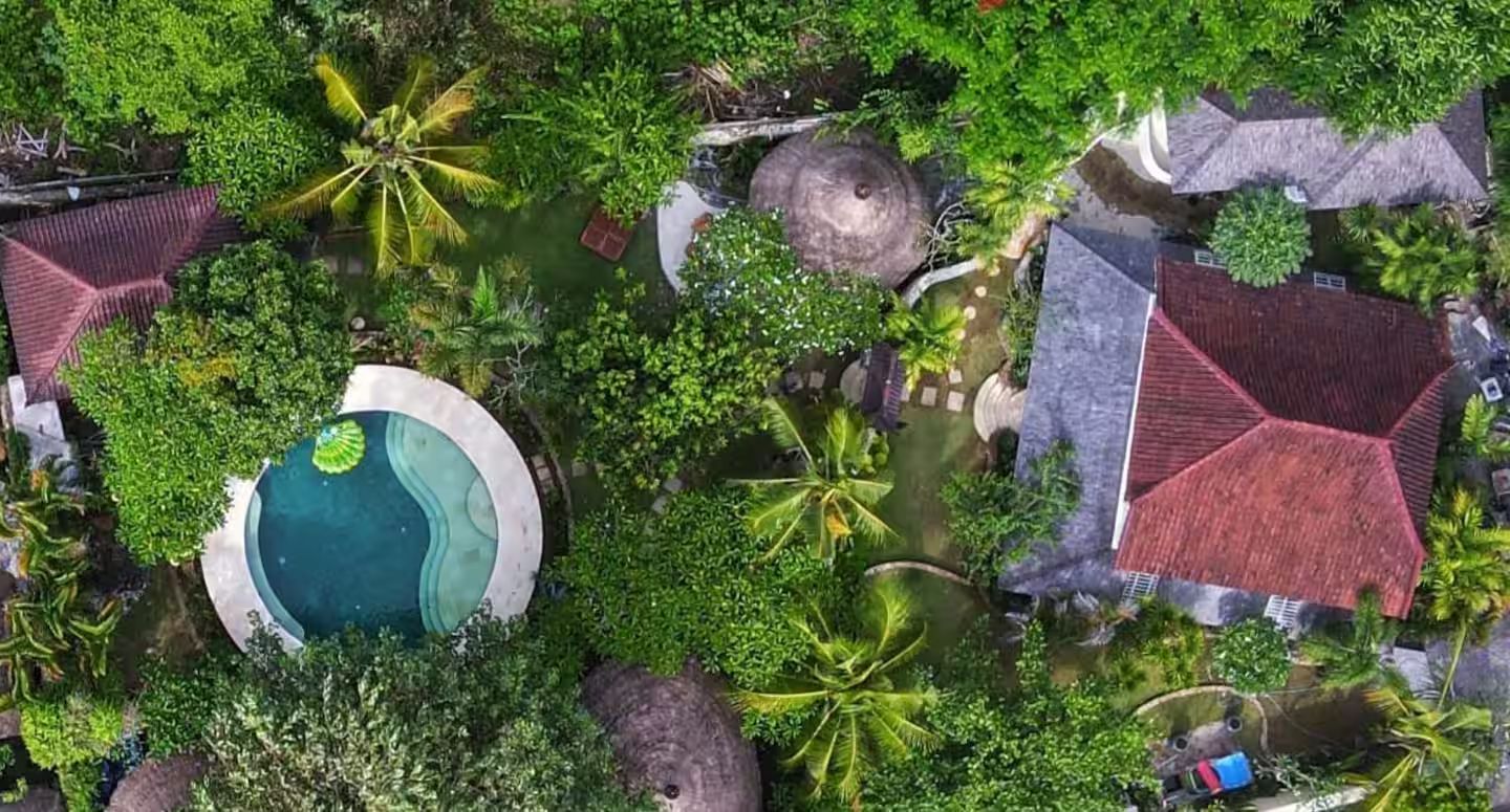 Aerial view of a tropical resort with a pool, lush greenery, and buildings with red and gray roofs.