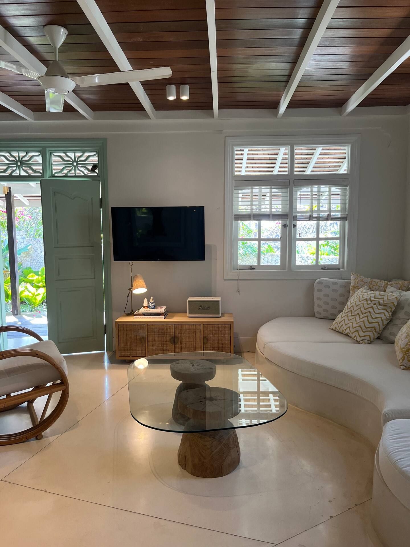Living room with white walls, a curved white sofa, and a glass coffee table. A TV is mounted above a wooden cabinet.