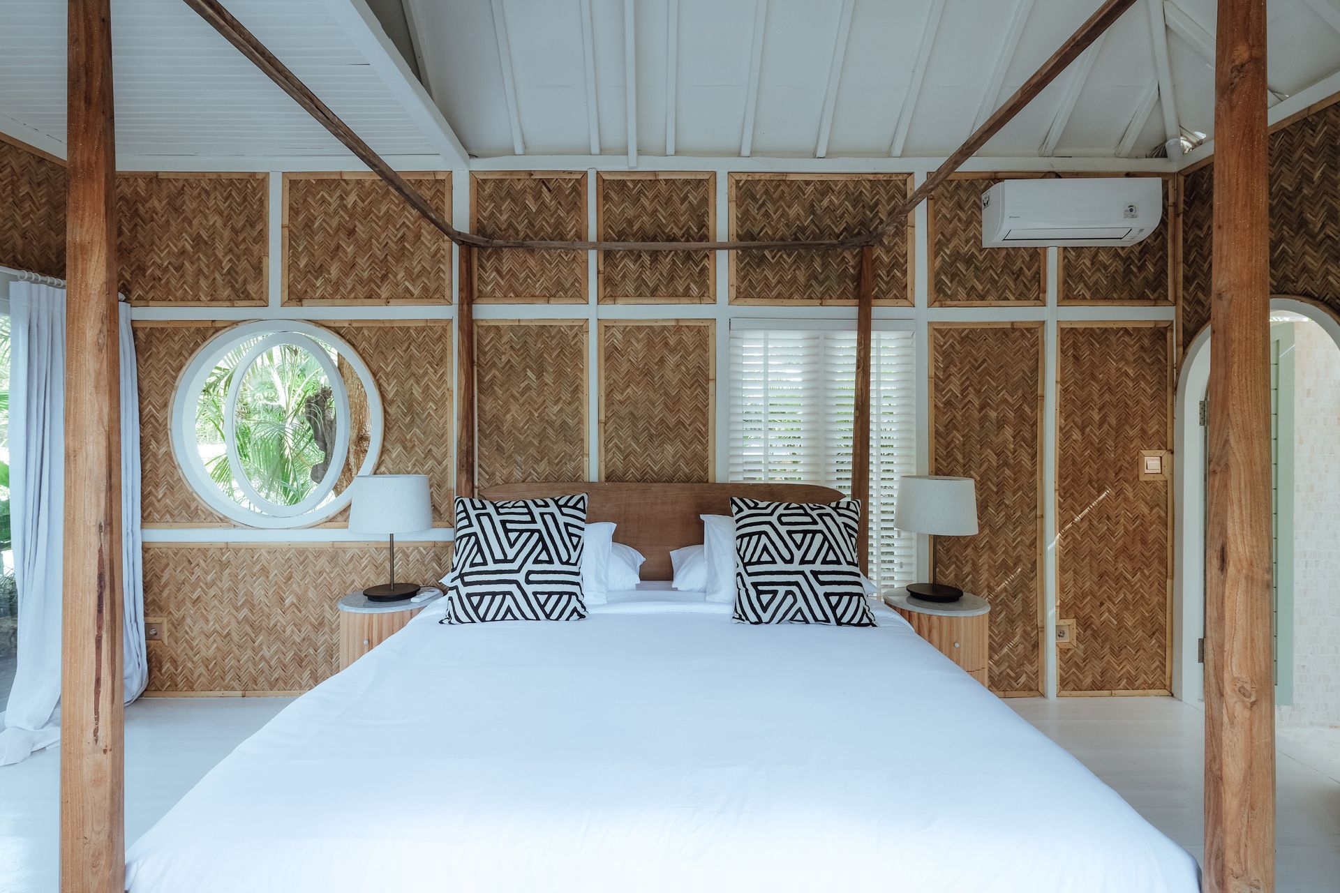 Bedroom with canopy bed, light wood accents, natural-looking walls, a round window, and black-and-white patterned pillows.