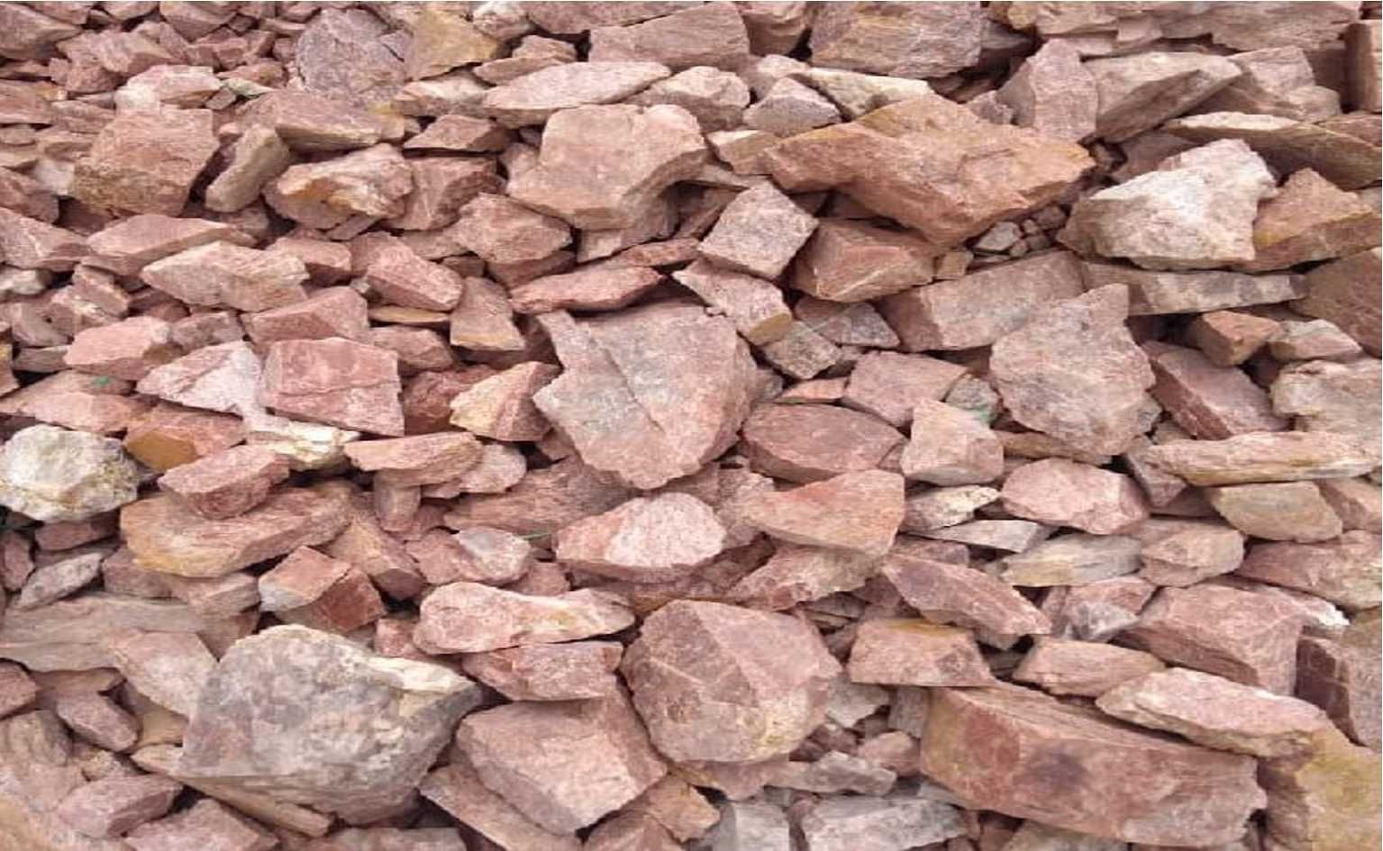 Montón de rocas de color marrón rojizo, de diversos tamaños y formas, posiblemente grava o fragmentos de piedra.