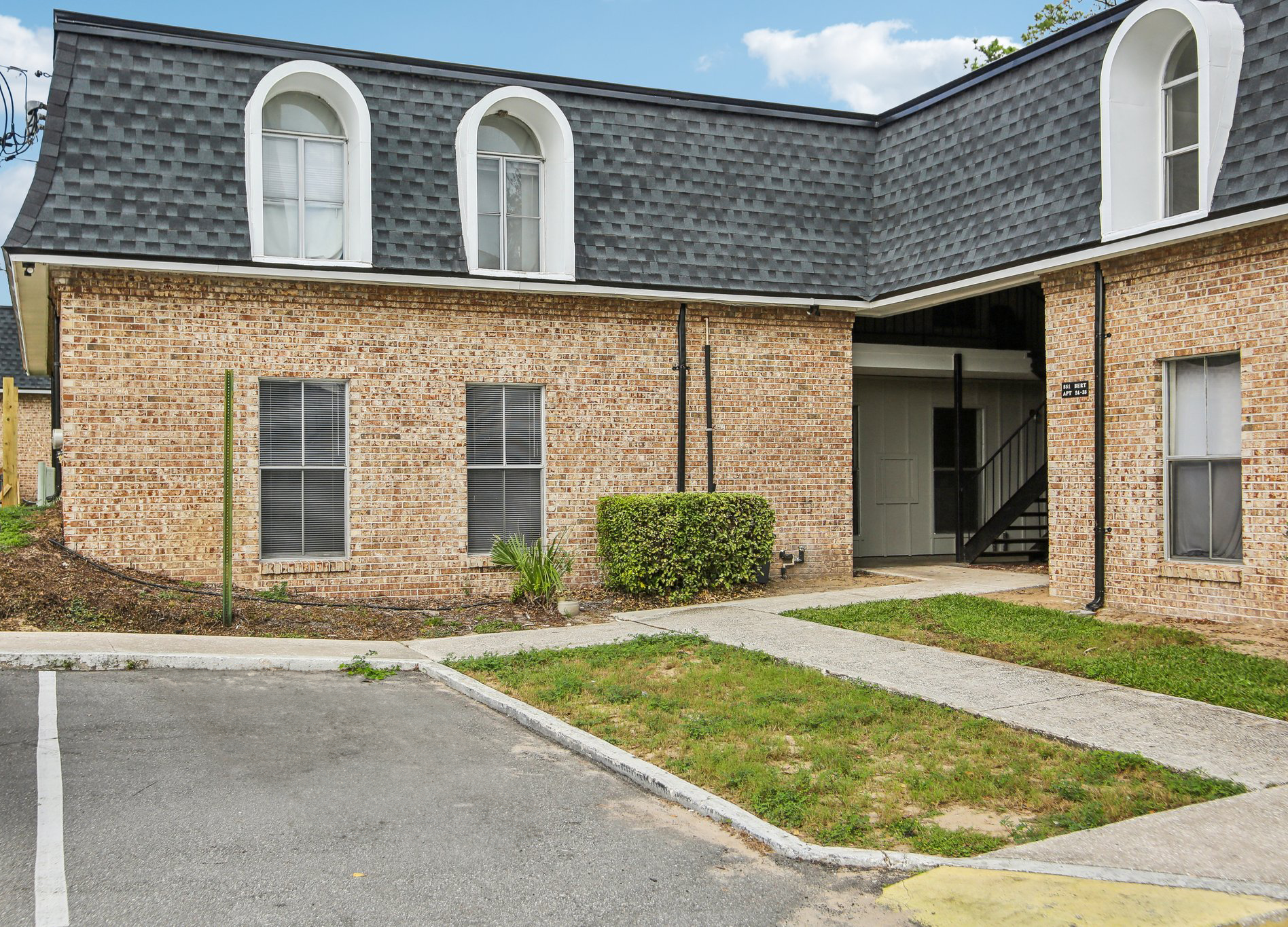 Apartment building with brick exterior, arched windows, and a black roof. A sidewalk leads to the entrance.