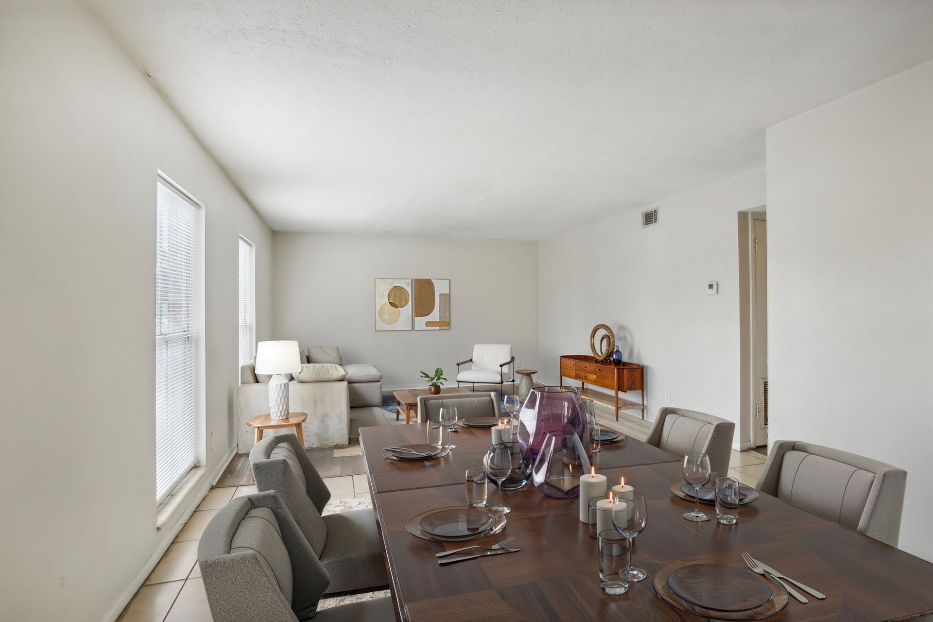 Dining room with long wooden table set for meal, and living room in background.