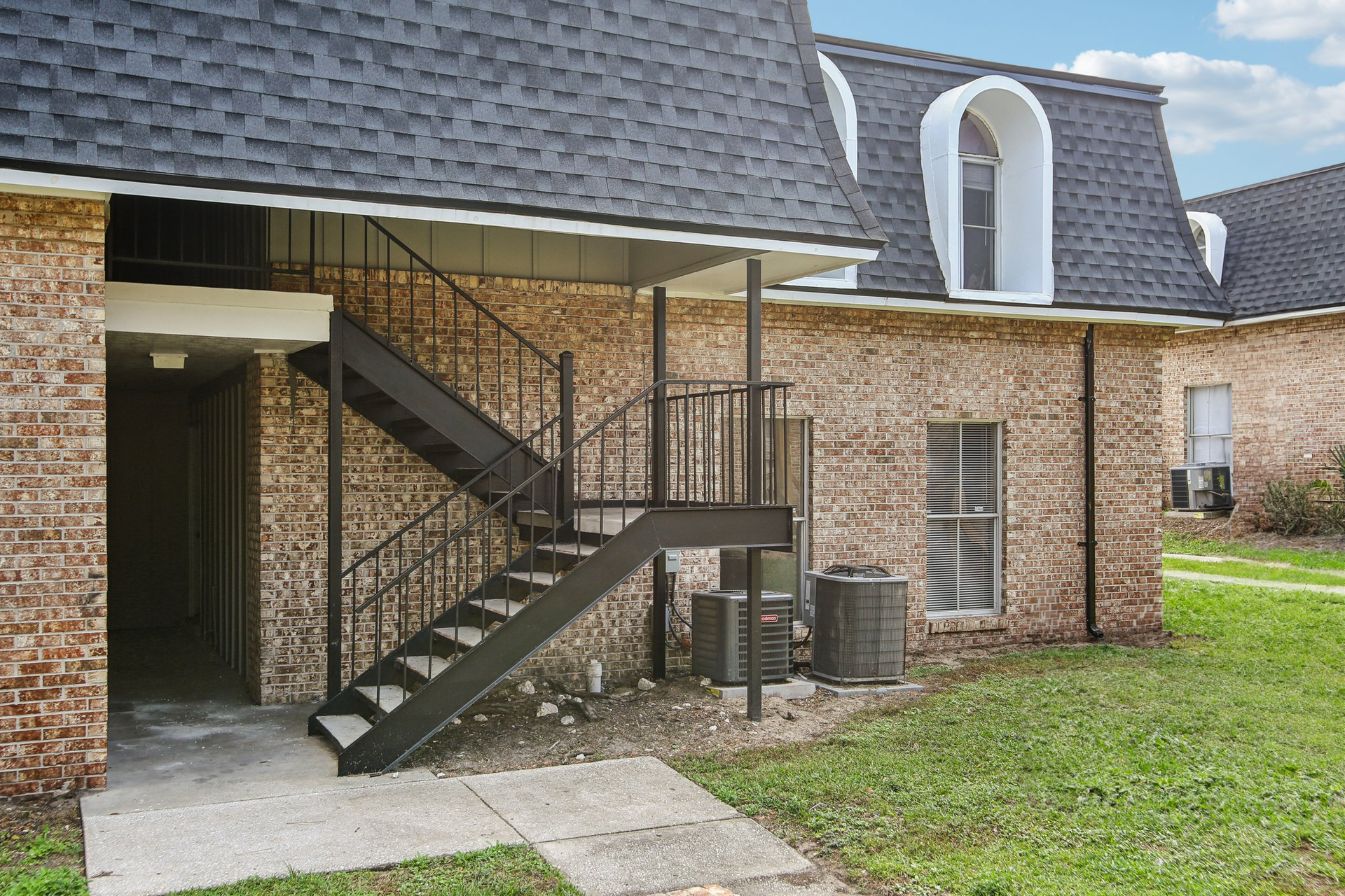 Exterior of brick apartment building with black staircase and dark roof.
