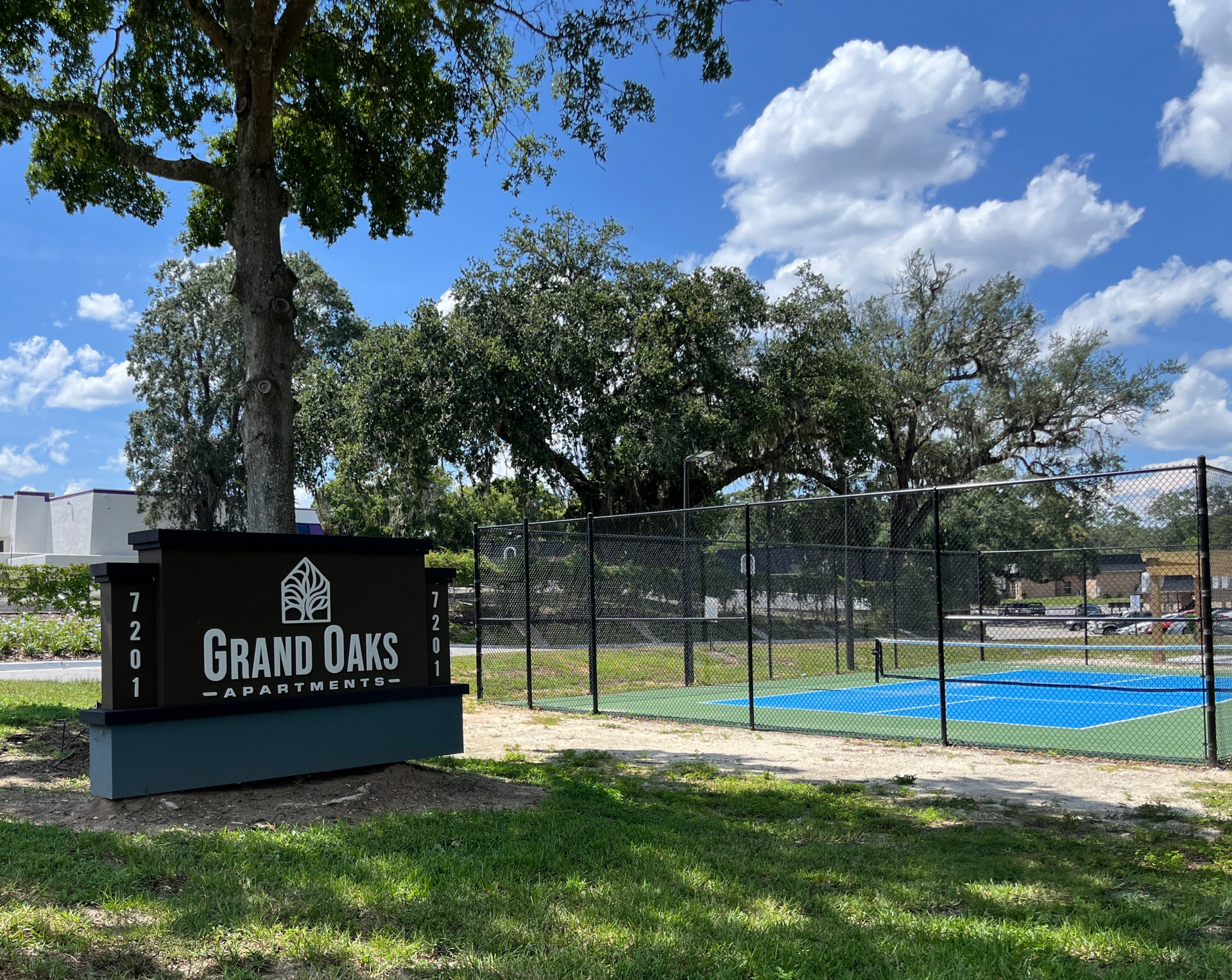 Sign for Grand Oaks Apartments in front of green lawn and blue court.
