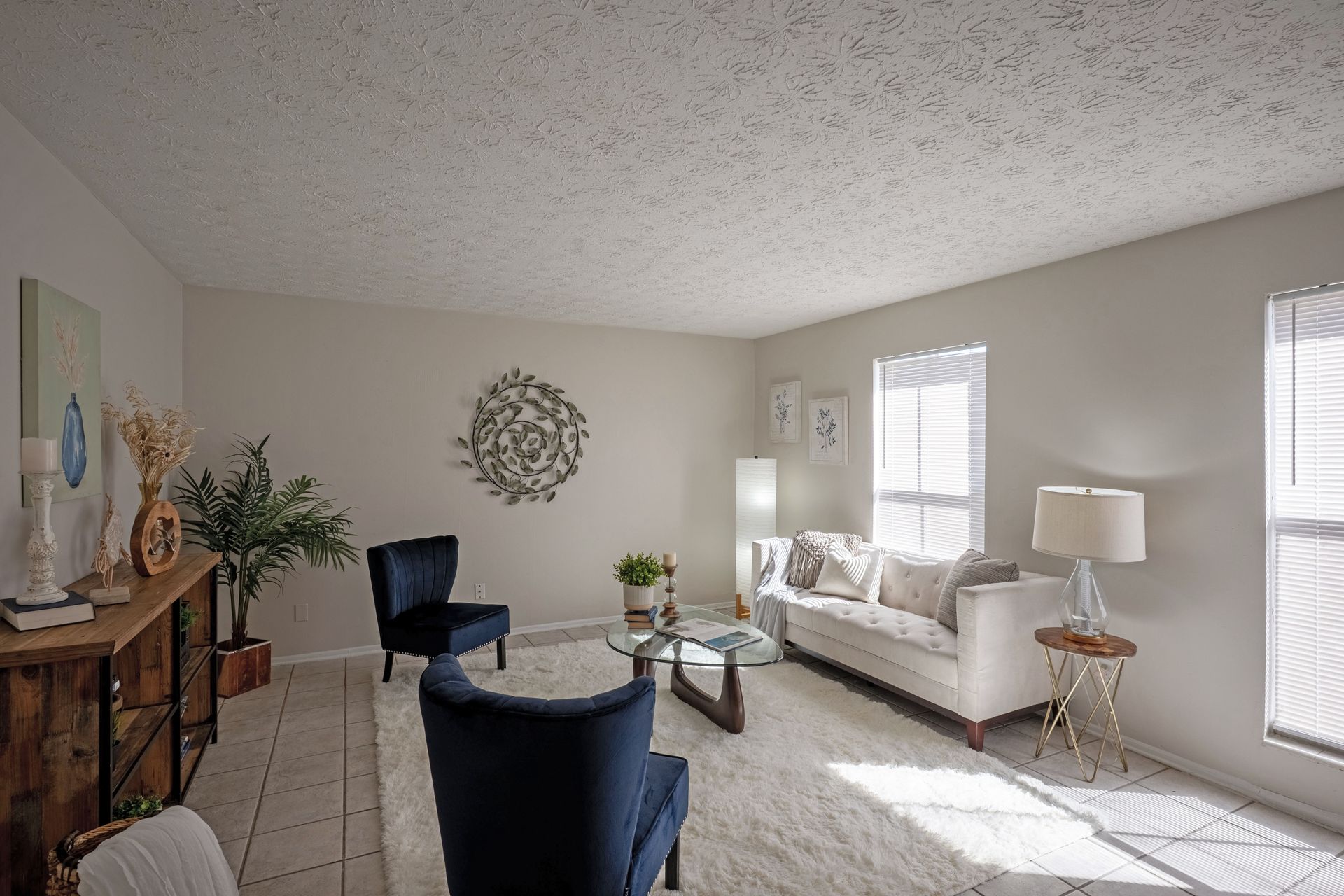 Living room with white walls, rug, couch, chairs, decor, and natural light.