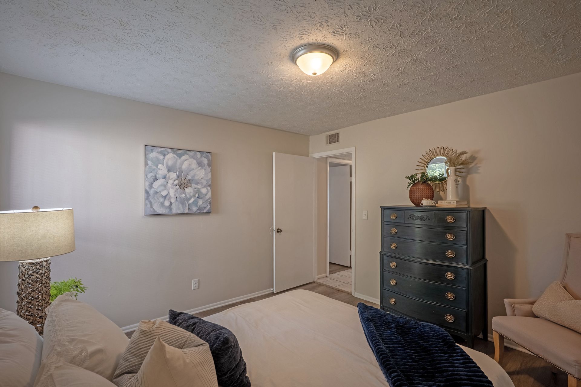 Bedroom with bed, dresser, chair, floral art, and doorway.