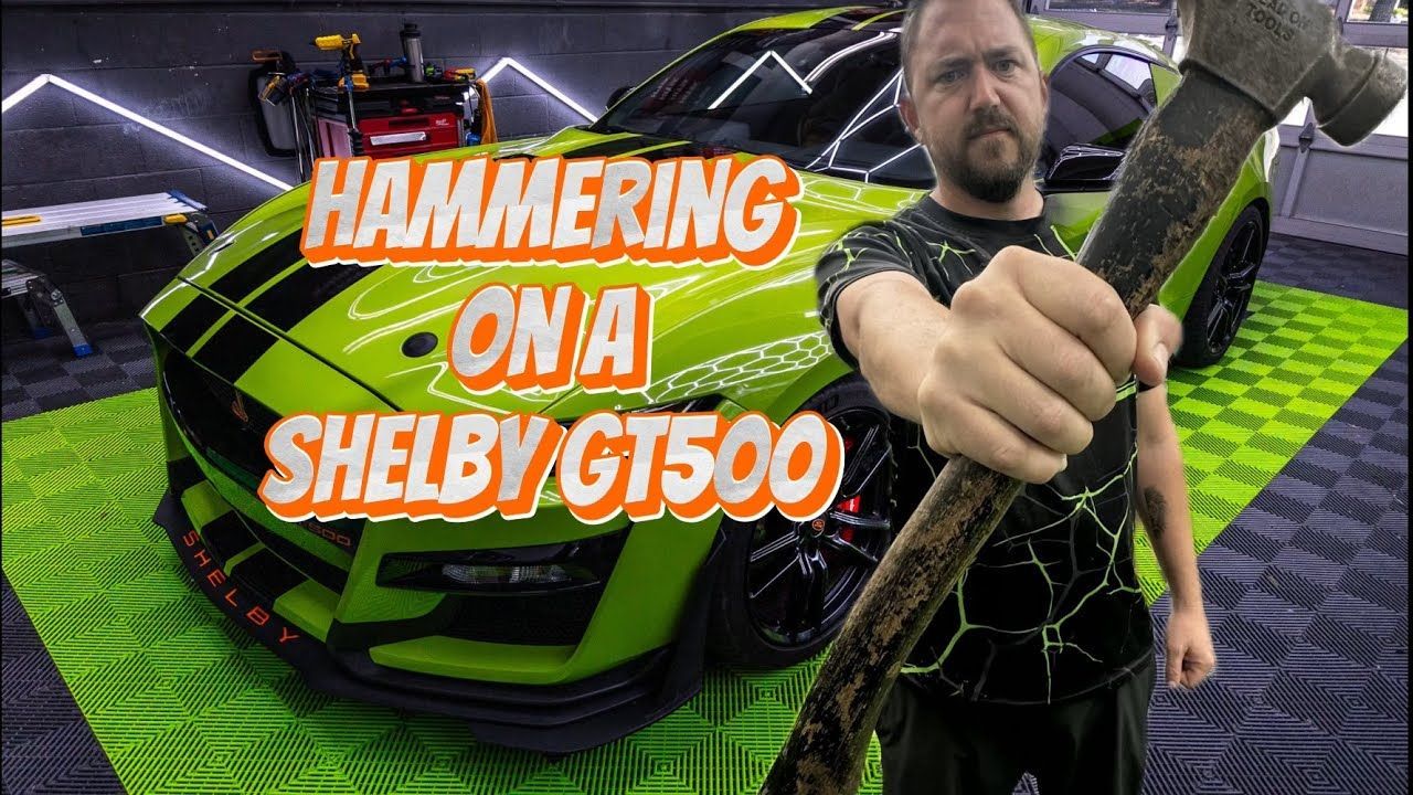 A man is holding a hammer in front of a green car.