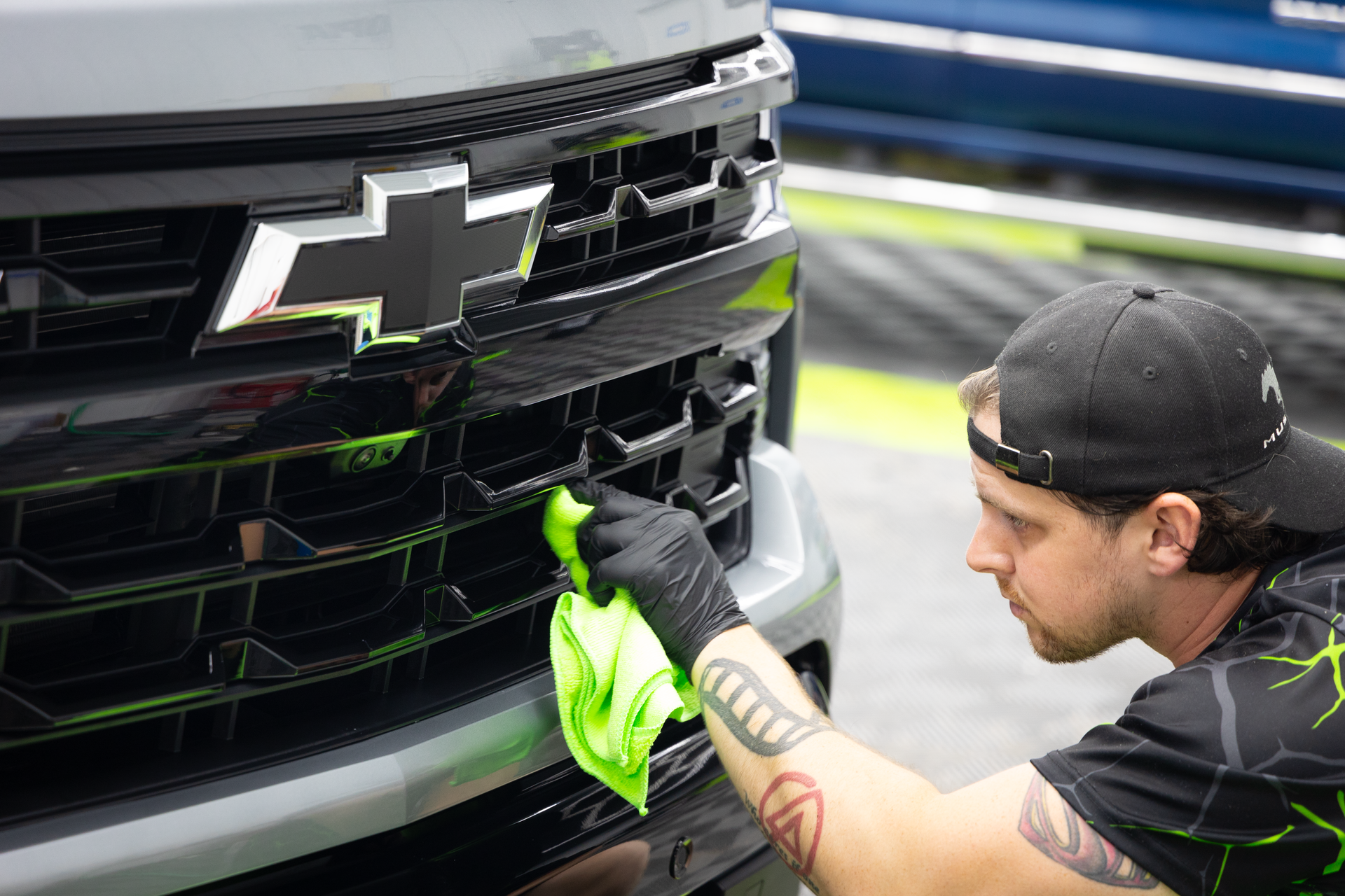 Man cleaning the front grill of a black Chevy truck with a green cloth.