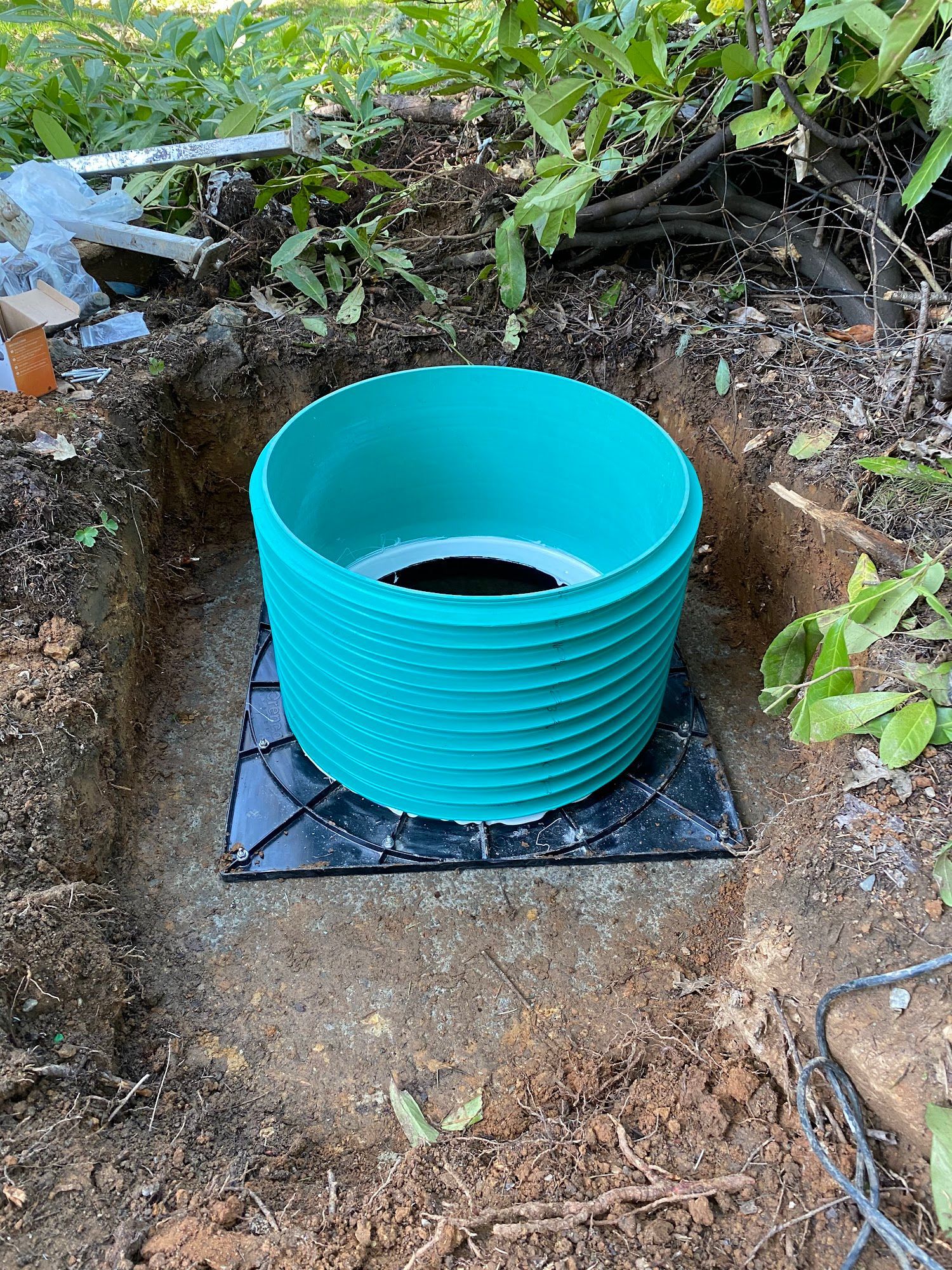 Green corrugated plastic cylinder in a square hole, set on a black grid, outdoors.