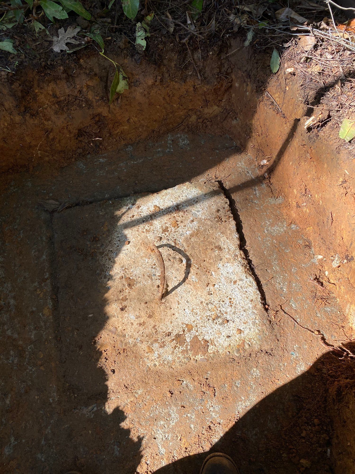 An open square hole in the ground reveals a rusty metal box with a D-shaped handle.