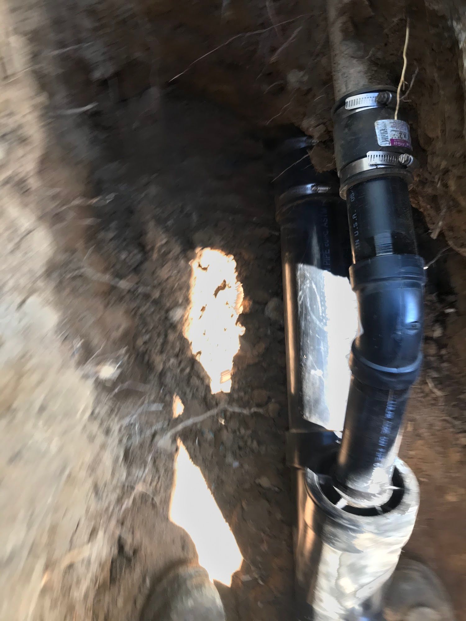 Black plumbing pipes in a dirt trench, likely for a drainage or sewer system.