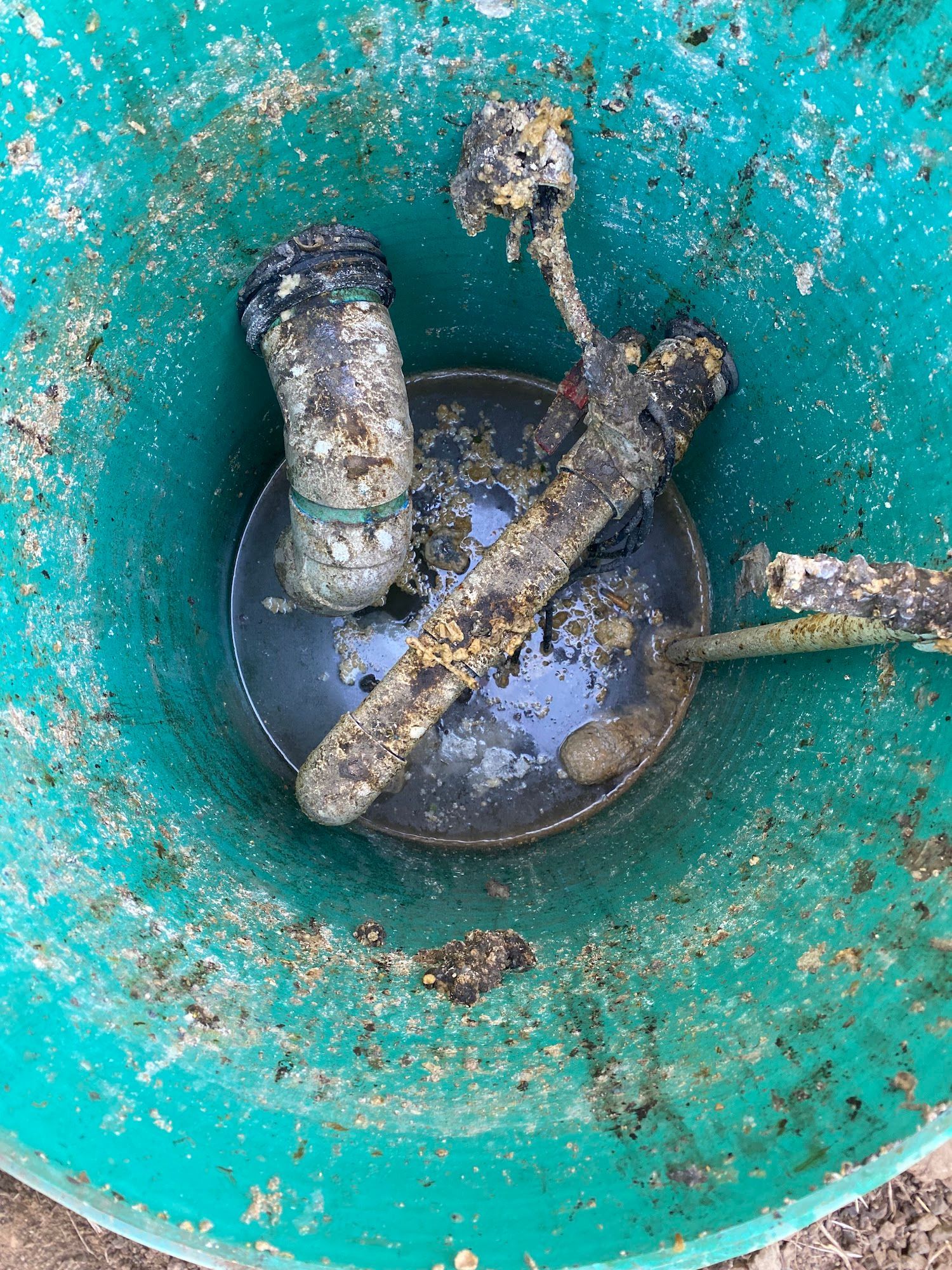 Top-down view of debris-filled bucket: includes gray PVC pipe, silverware, all covered in organic matter.