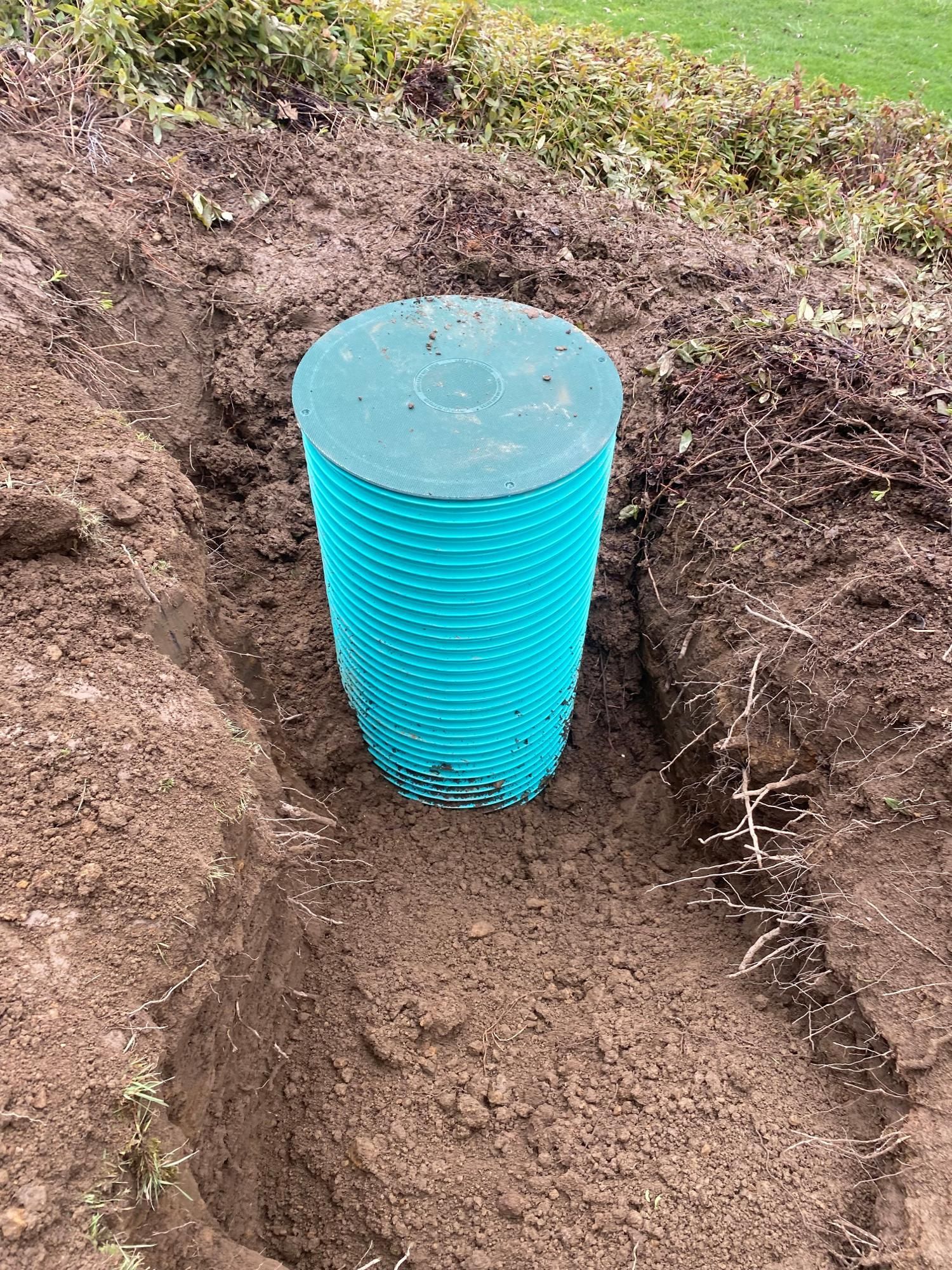 Green, cylindrical structure in a trench, with a green lid, in an outdoor setting.