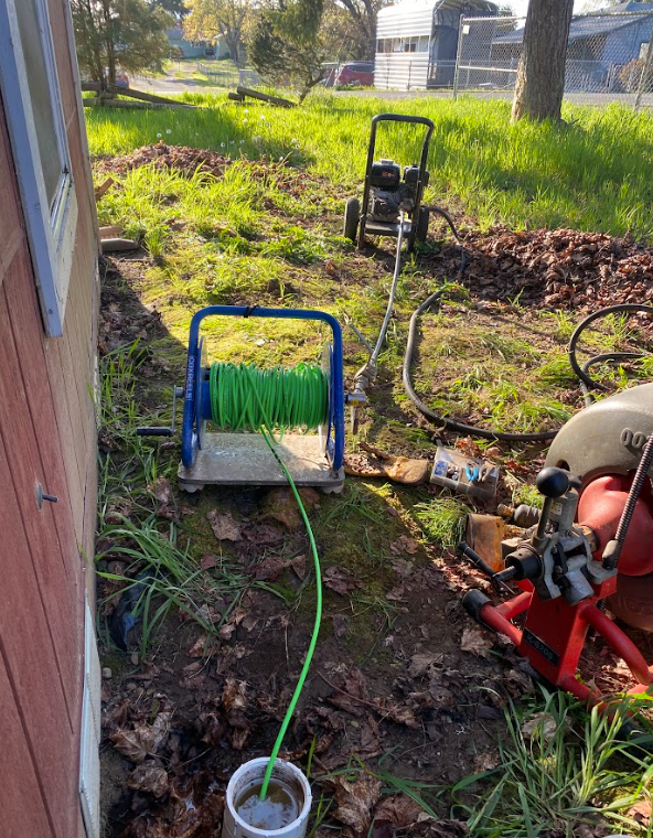 Green hose on blue reel filling a white bucket outdoors beside a brick wall and yard equipment.