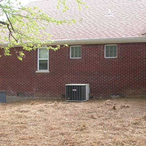 A brick house with a air conditioner in the backyard.
