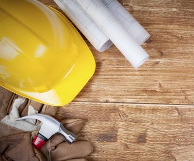 A hard hat , gloves , a hammer , and blueprints are on a wooden table.