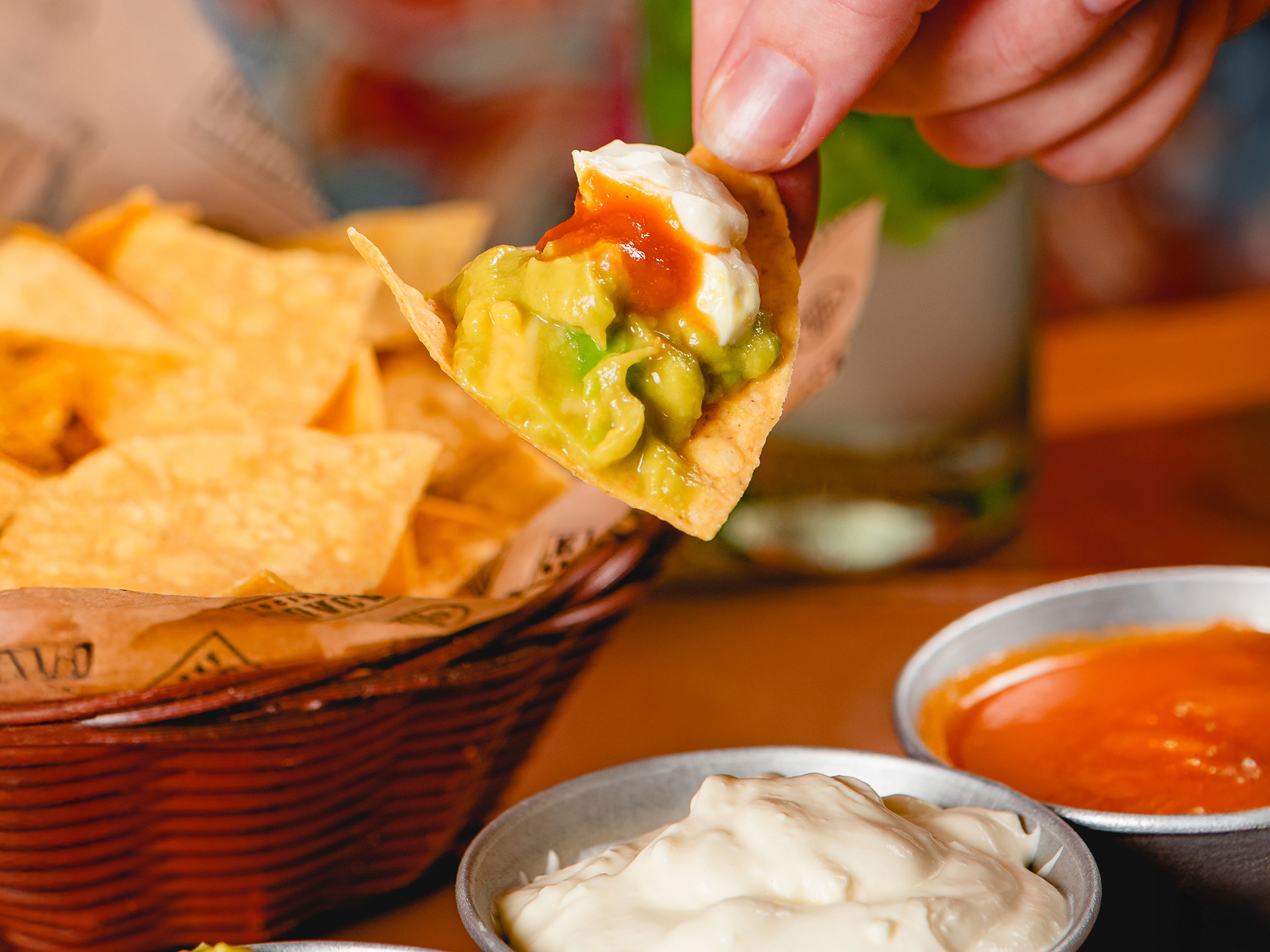 Mergulhando um nacho na guacamole, com tigelas de nachos e salsa por perto.